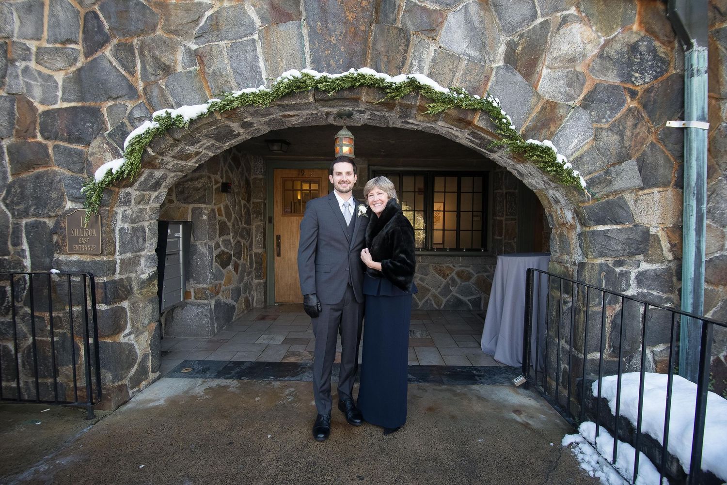 Couple posing under a snow-dusted stone arch at a winter wedding venue.