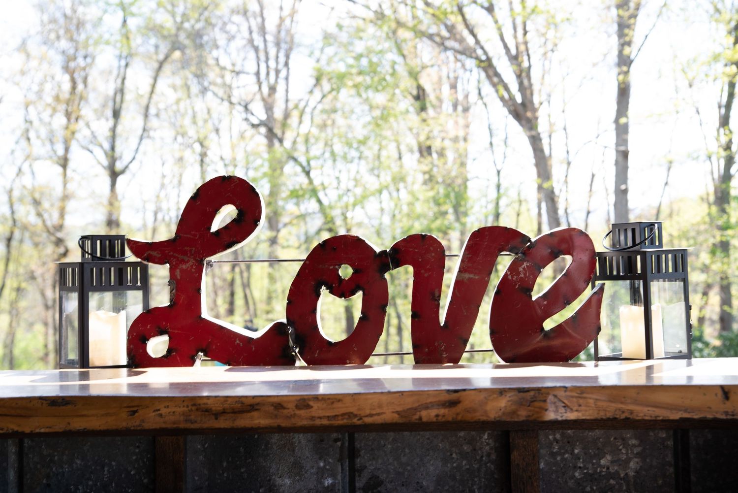 Decorative red metal Love sign displayed on a wooden table with glass lantern centerpieces at a wedding reception.