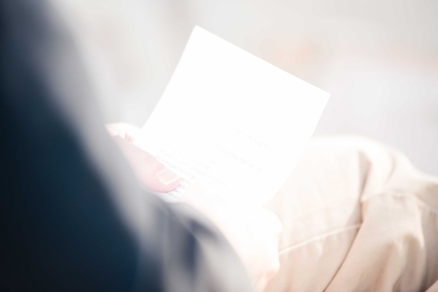 Person holding a bright white card or letter in soft natural light, wearing a light beige outfit.