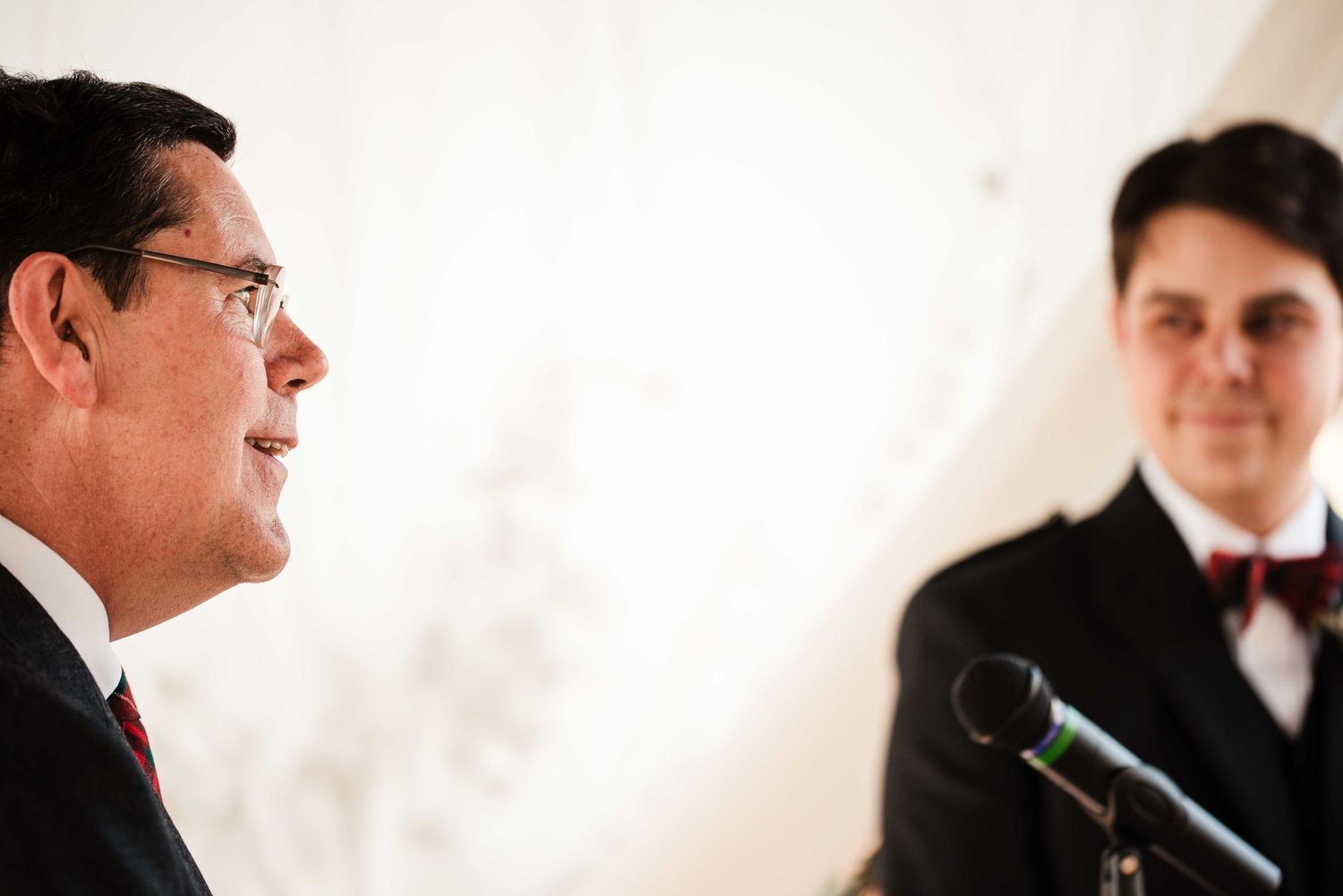 Two men in formal suits speak at a microphone during an official press conference or formal event.