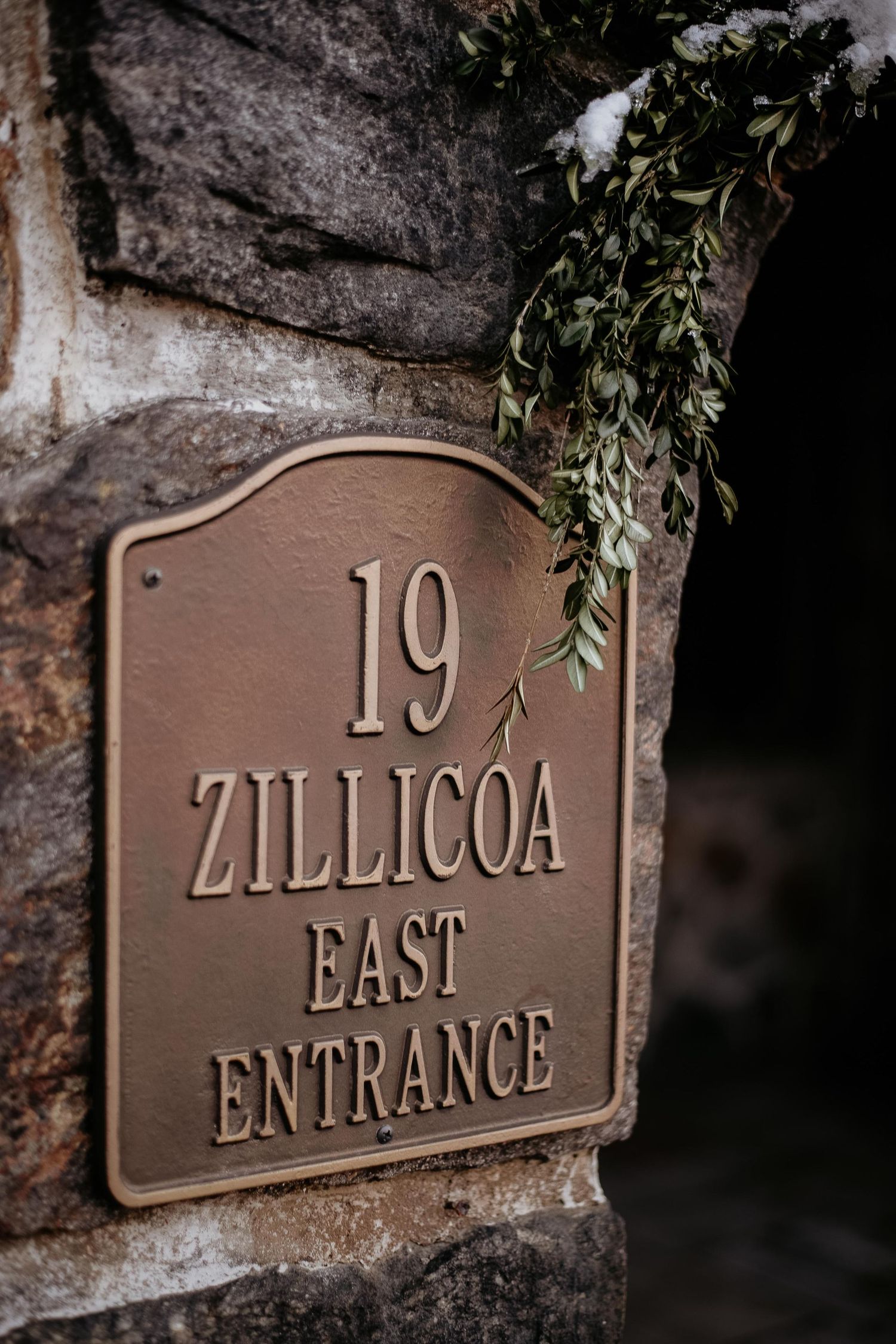 Bronze address sign reading 19 Zillicoa East Entrance mounted on stone wall with green foliage decoration.