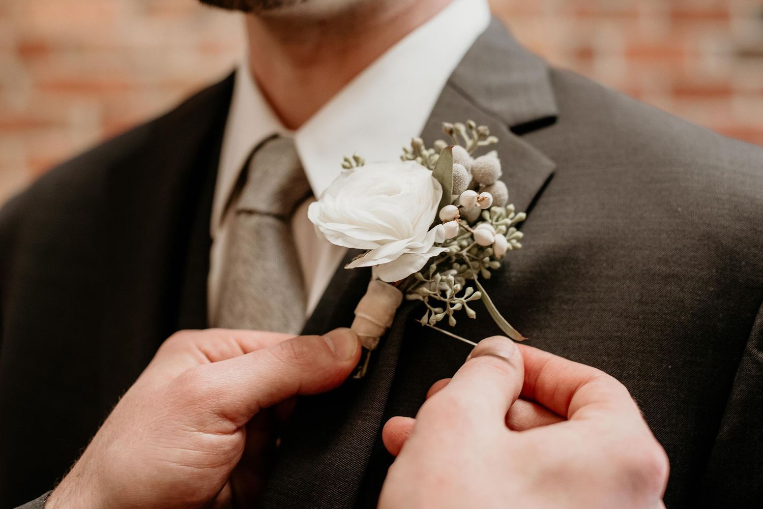 Groom having a white floral boutonniere pinned to his dark suit lapel on his wedding day.