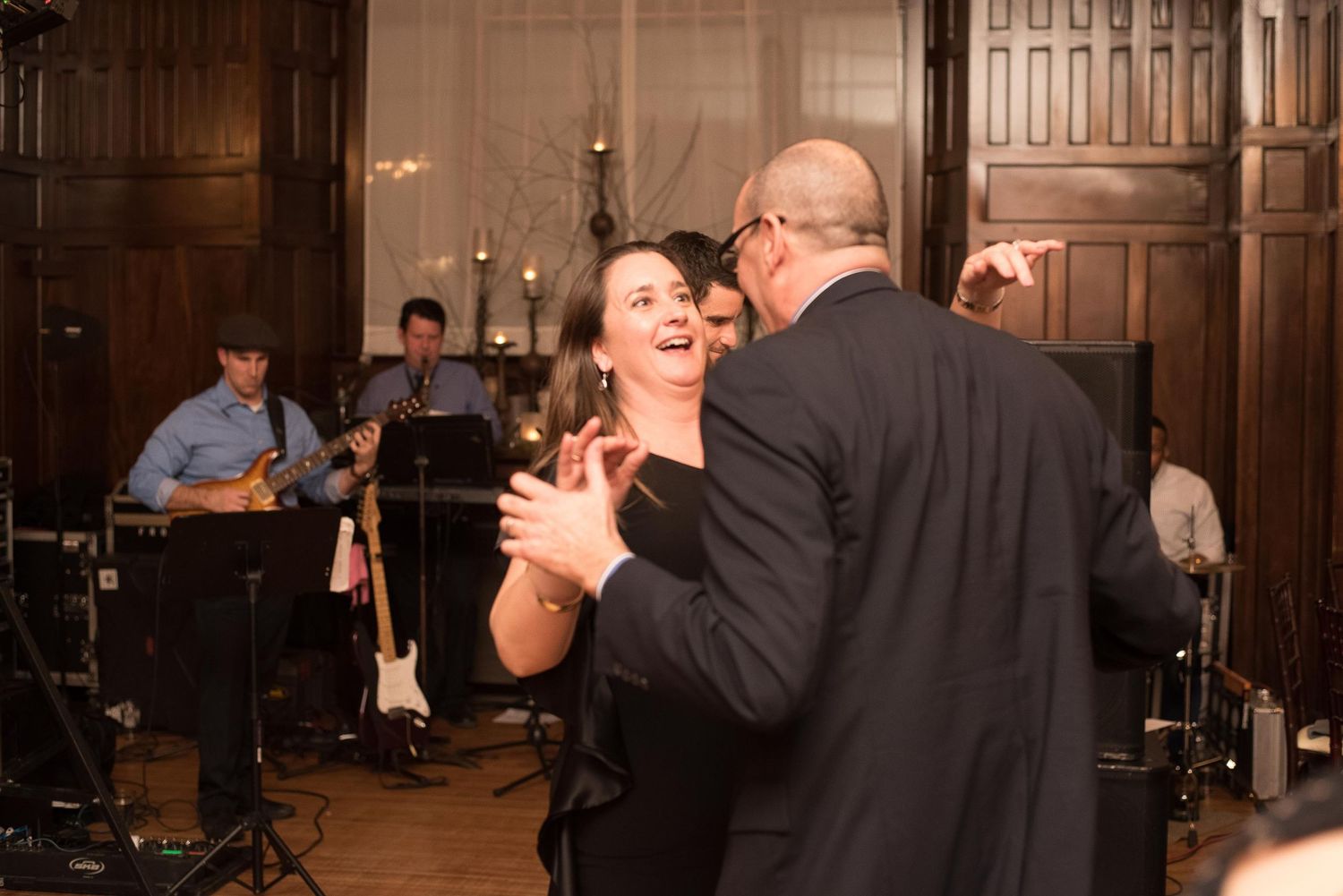 Couple dancing joyfully at elegant wedding reception with live band performing in background.