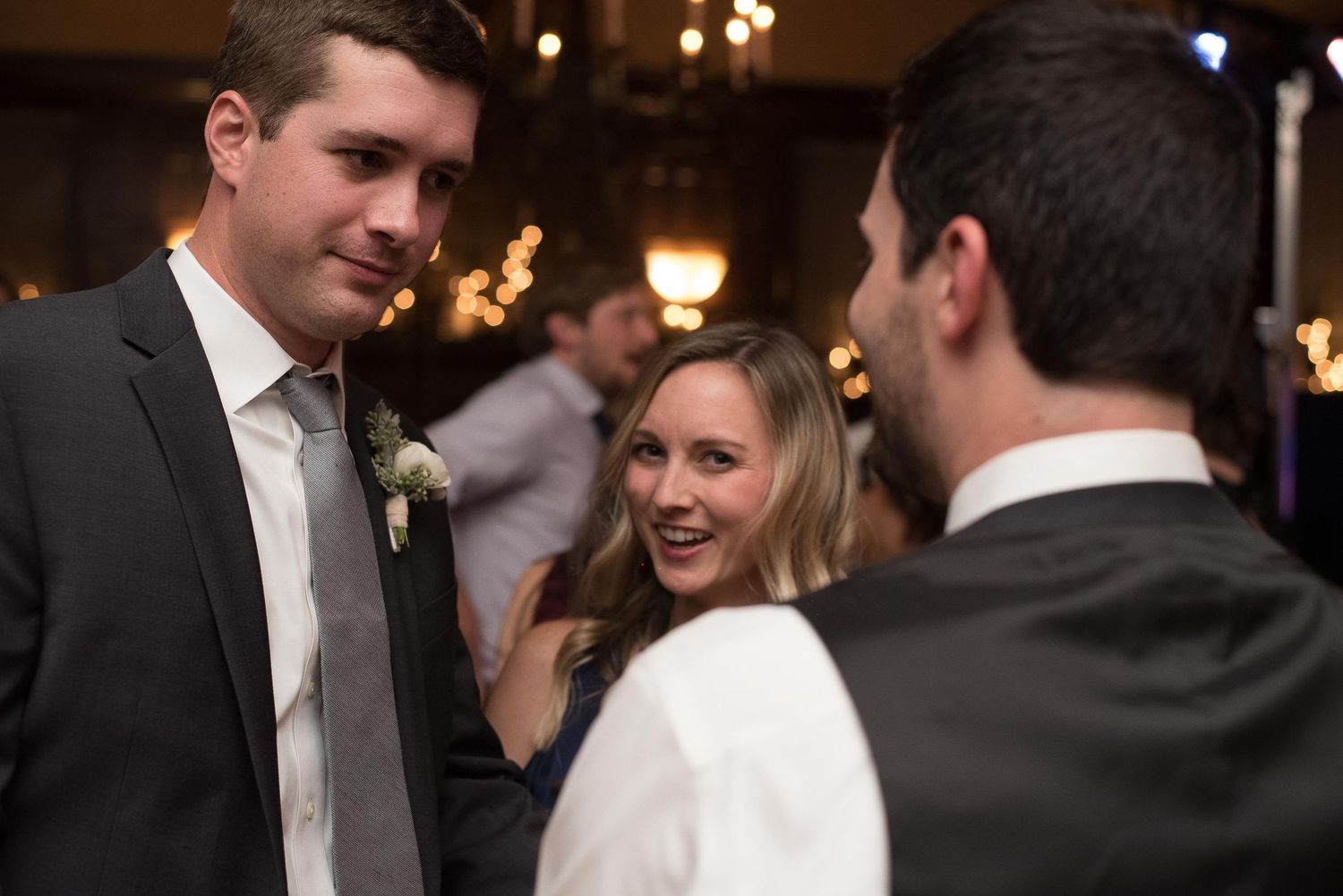 Three elegantly dressed guests socializing at a formal wedding reception in a warmly lit venue.