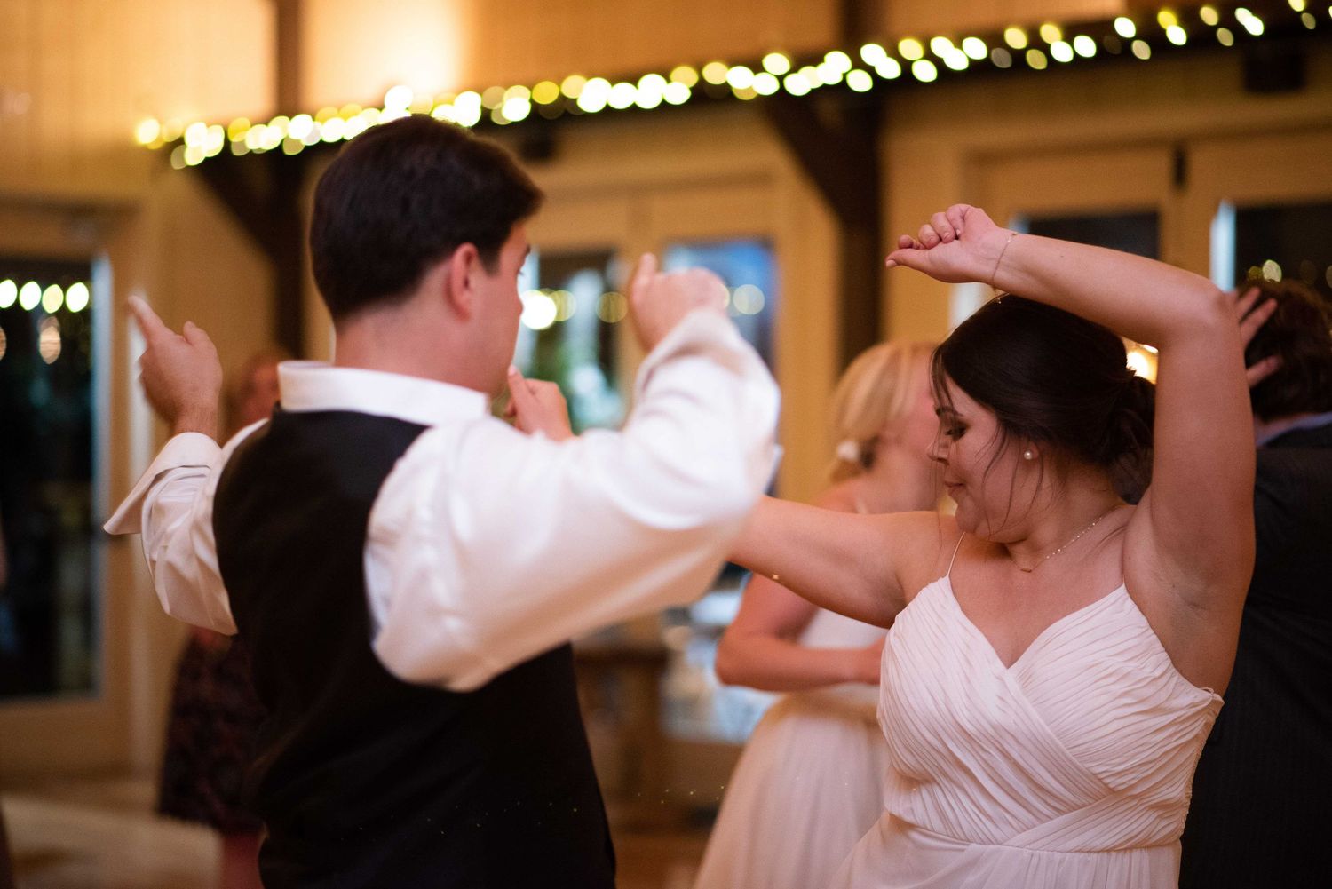 Bride and groom dancing together at wedding reception with warm bokeh lights in background.