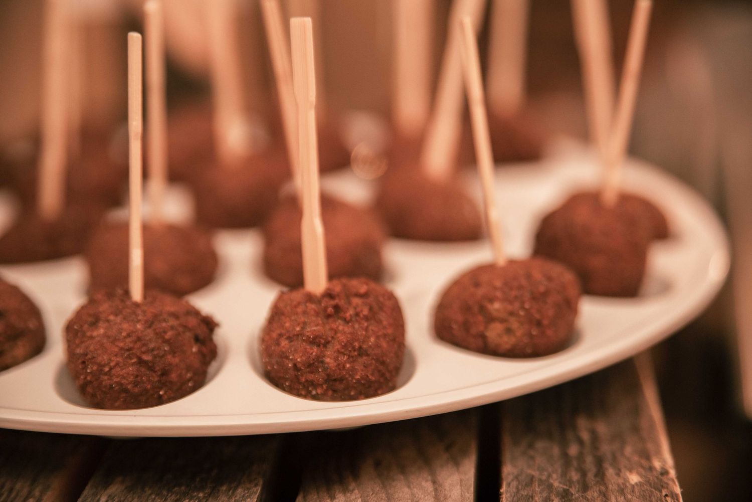 Chocolate truffles with wooden toothpick skewers arranged on a white oval serving platter.