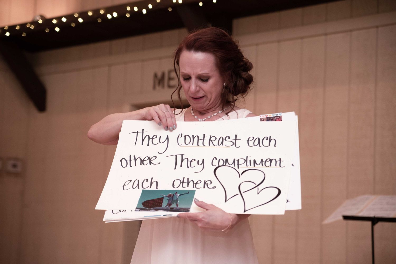 Woman in white dress holding a sign reading They contrast each other, They compliment each other at a wedding reception.