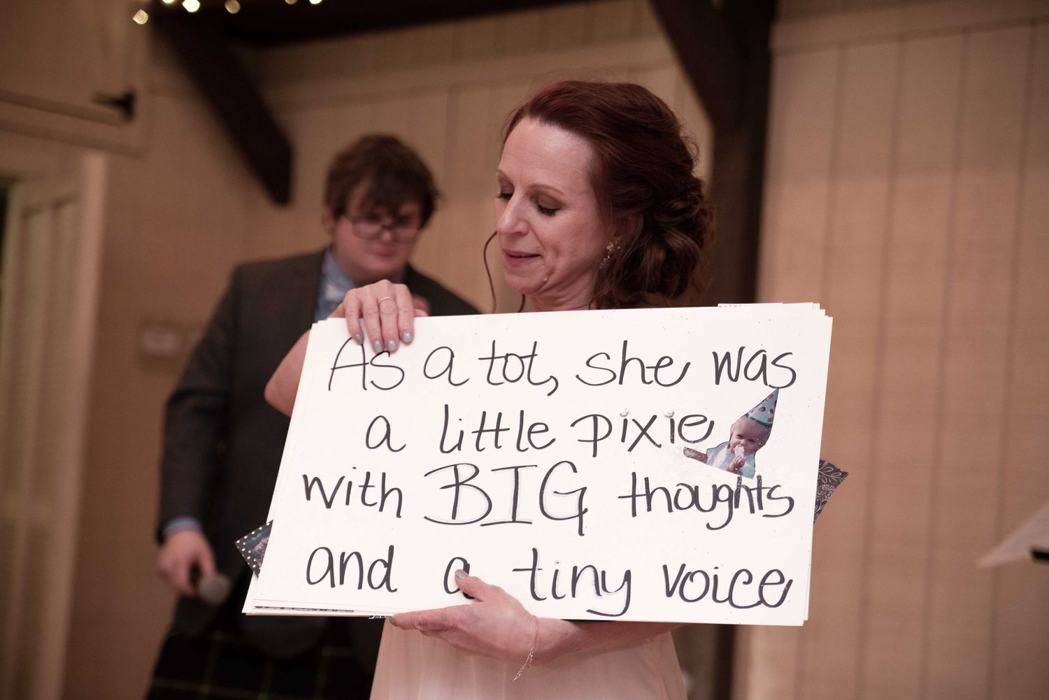 Woman in wedding dress holds sign reading as a tot she was a little pixie with big thoughts and a tiny voice.