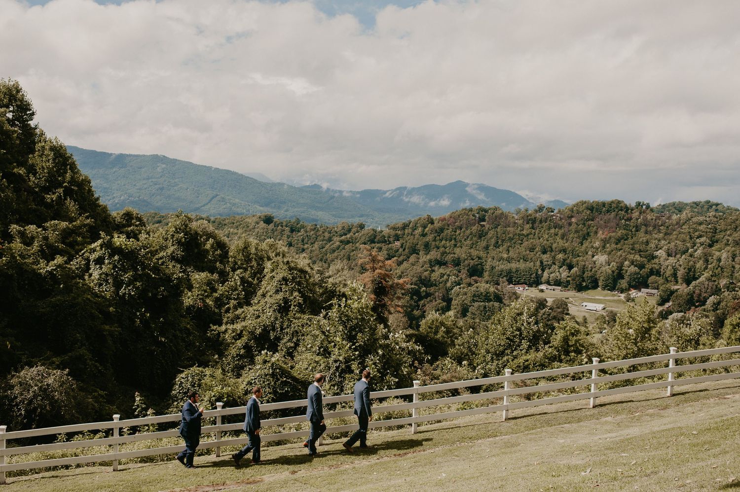 Groomsmen walking along a white fence with stunning mountain landscape views.