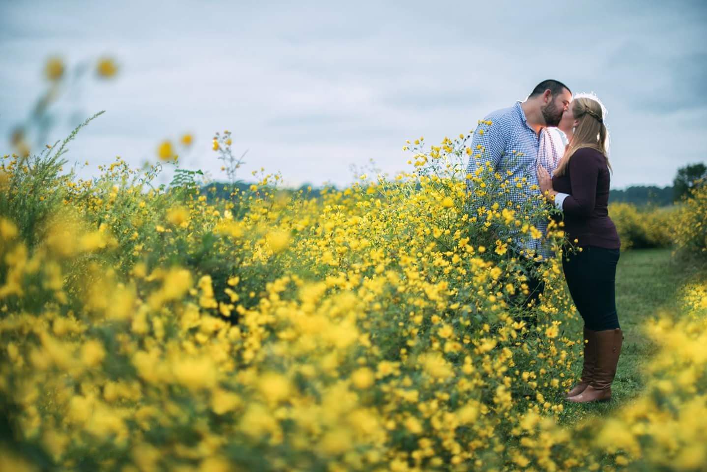 Romantic couple sharing a kiss in vibrant yellow wildflower field during outdoor engagement session.