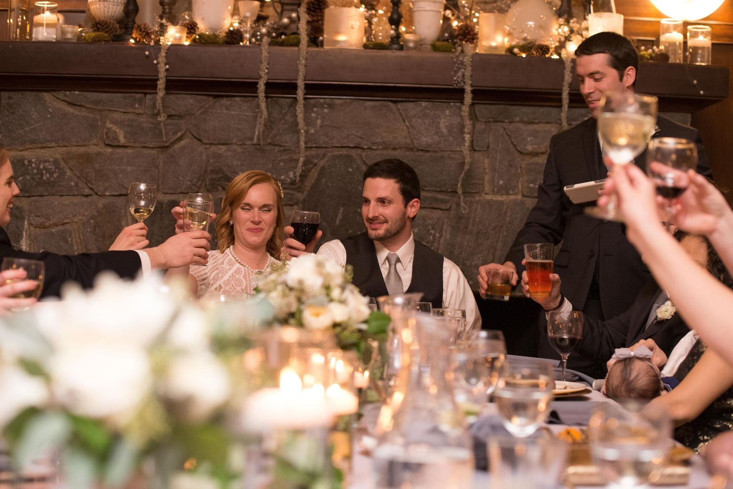 Guests raising glasses in a toast at an elegant wedding reception dinner with candlelight and floral centerpieces.