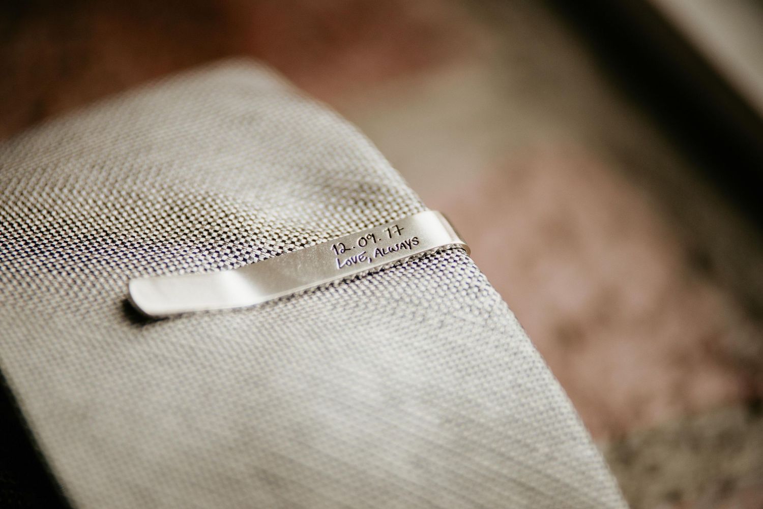 Close-up of a light gray linen tie with a small personalized label, perfect for a wedding or formal occasion.