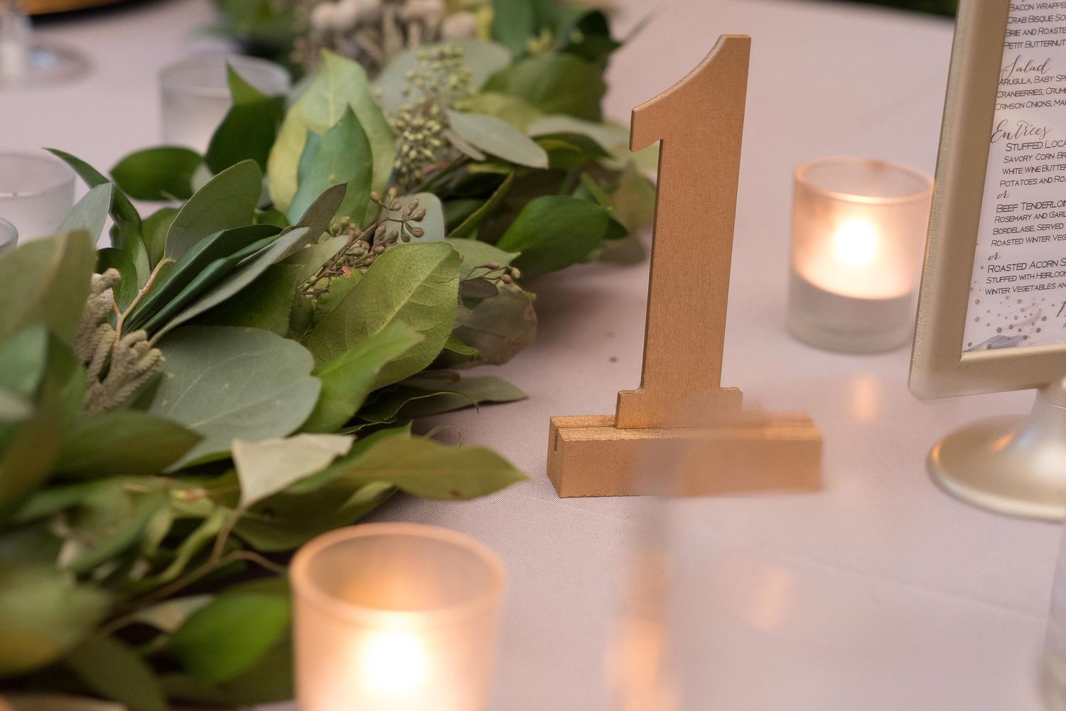 Gold number one table marker surrounded by greenery and glowing candles at an elegant wedding reception.