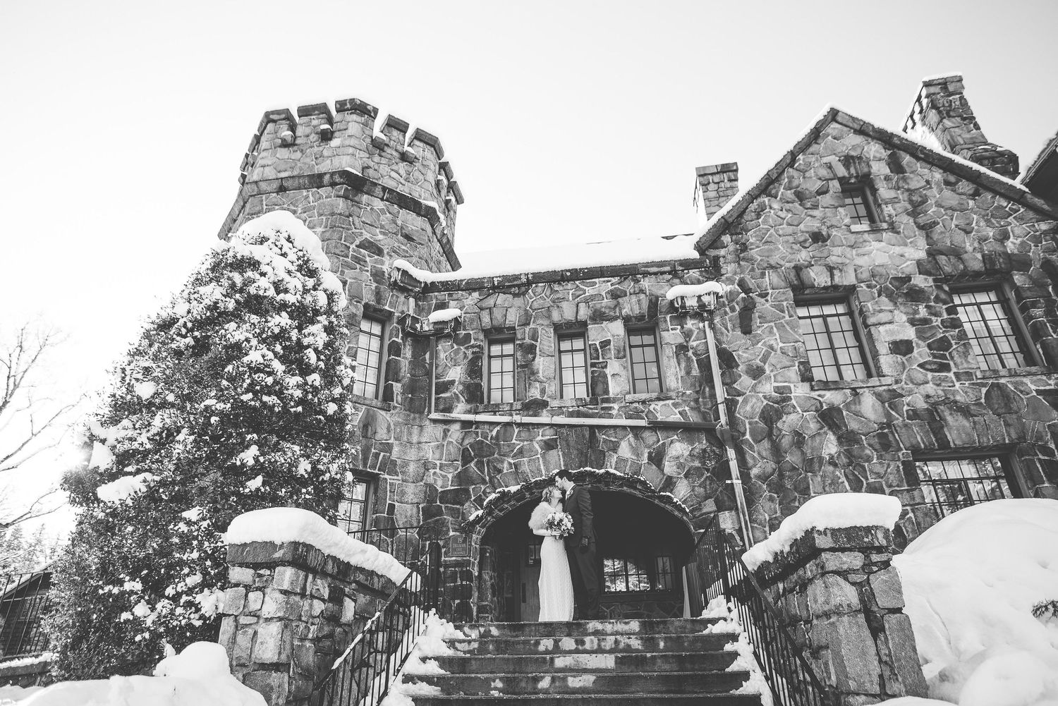Bride and groom pose on snowy castle steps in a romantic black and white winter wedding photo.