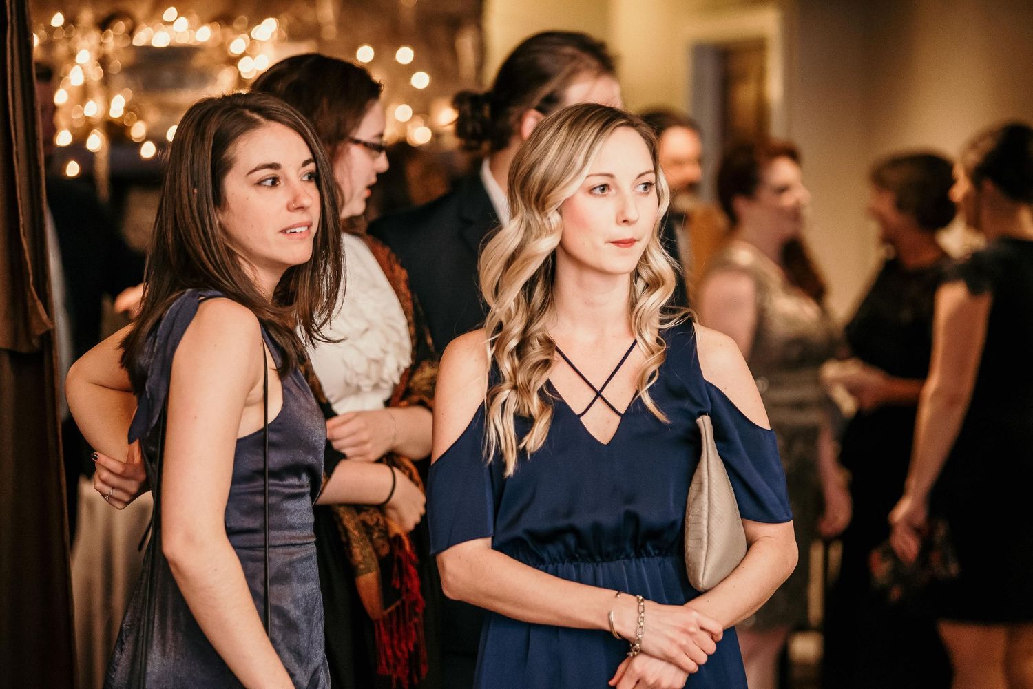 Two women in navy blue dresses at an elegant evening event, standing together in a warmly lit venue.