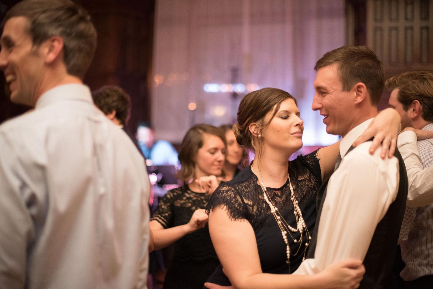 Couple slow dancing at a wedding reception, woman in black lace dress with arm around man in white shirt.