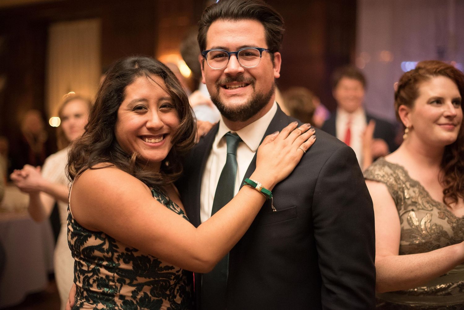 Couple smiling and posing together at a formal event, man in suit with green tie, woman in dark dress.