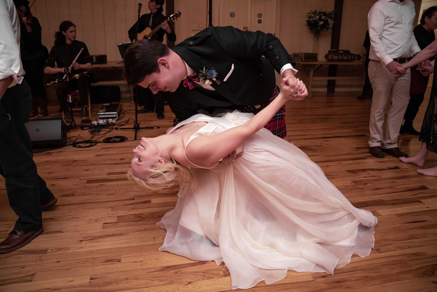 Bride and groom sharing a dramatic dip dance move on wooden dance floor at wedding reception.