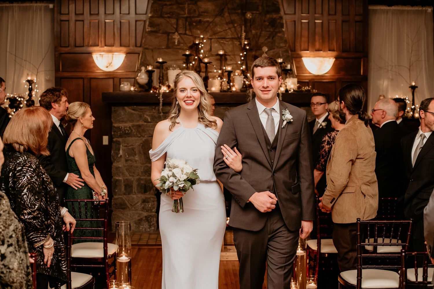 Bride and groom walk down the aisle smiling after wedding ceremony in elegant wood-paneled venue.