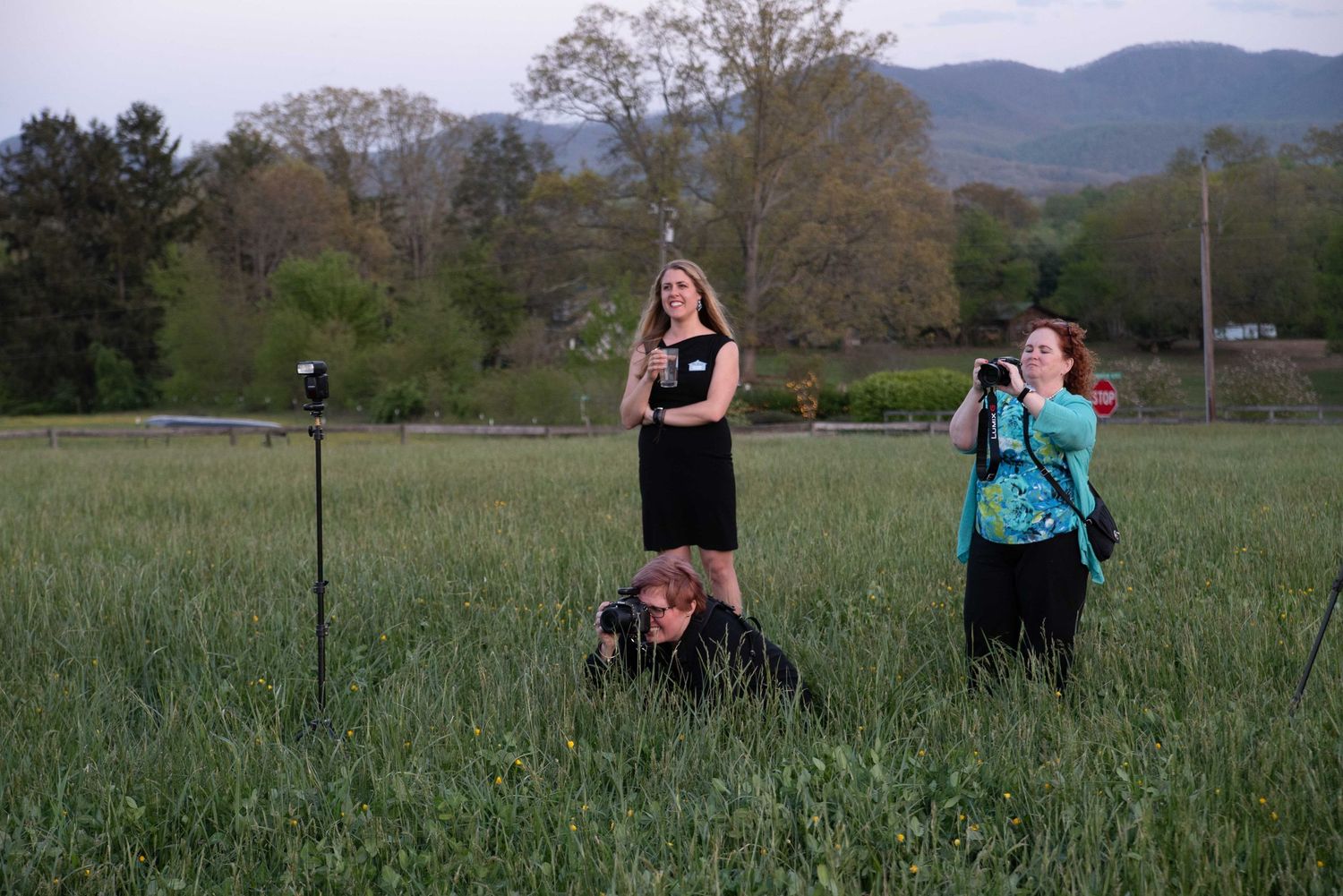 Three photographers working in a lush green field with mountains in the background at dusk.