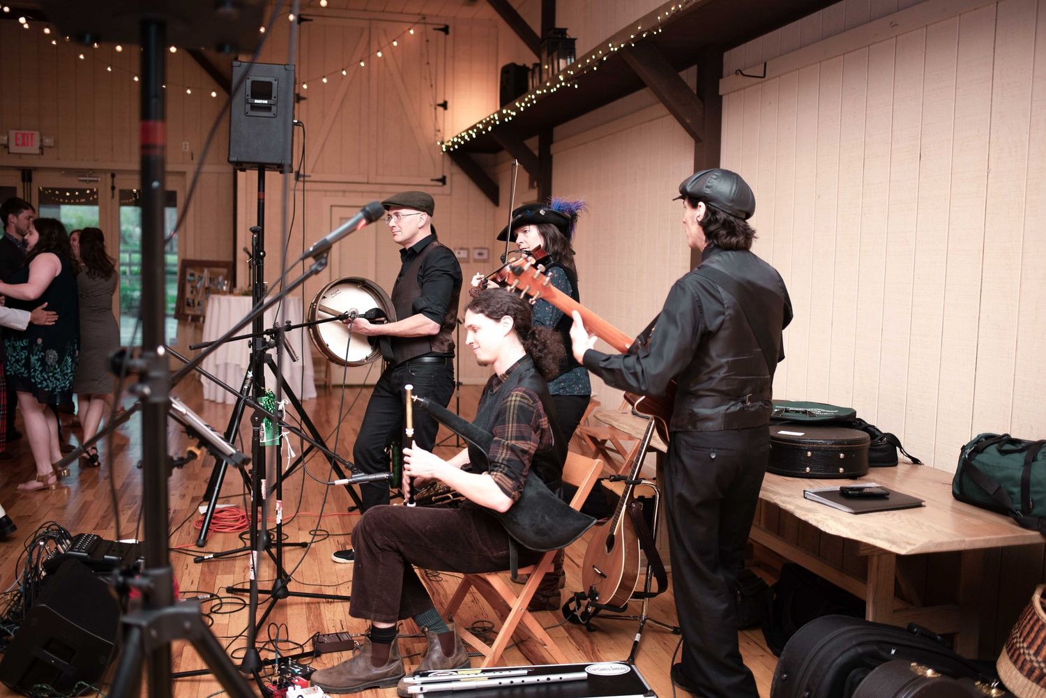 Band performing folk music indoors at a rustic venue with string lights, musicians playing banjo and guitar on stage.