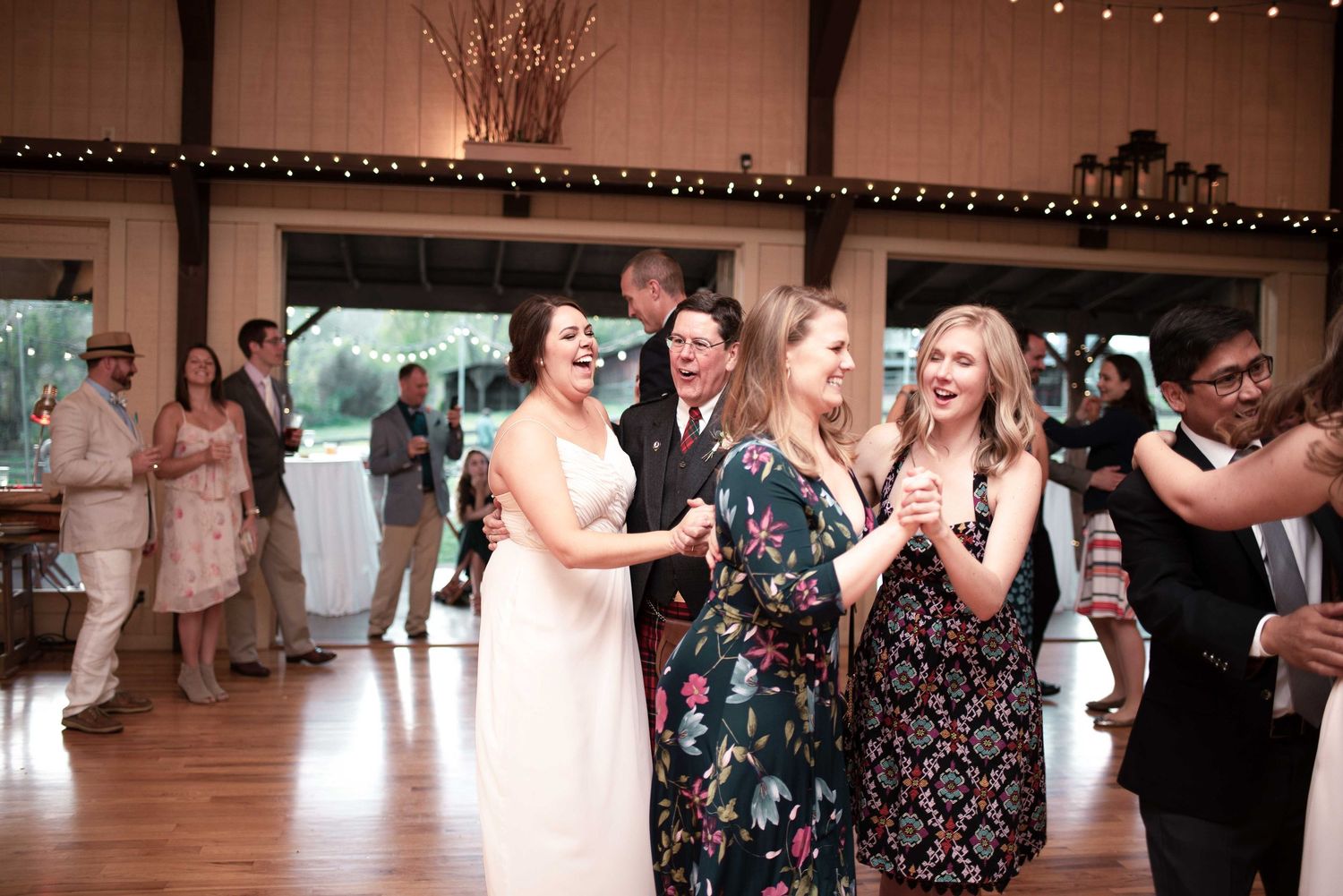 Guests dancing and laughing at a rustic wedding reception in a warmly lit barn venue.