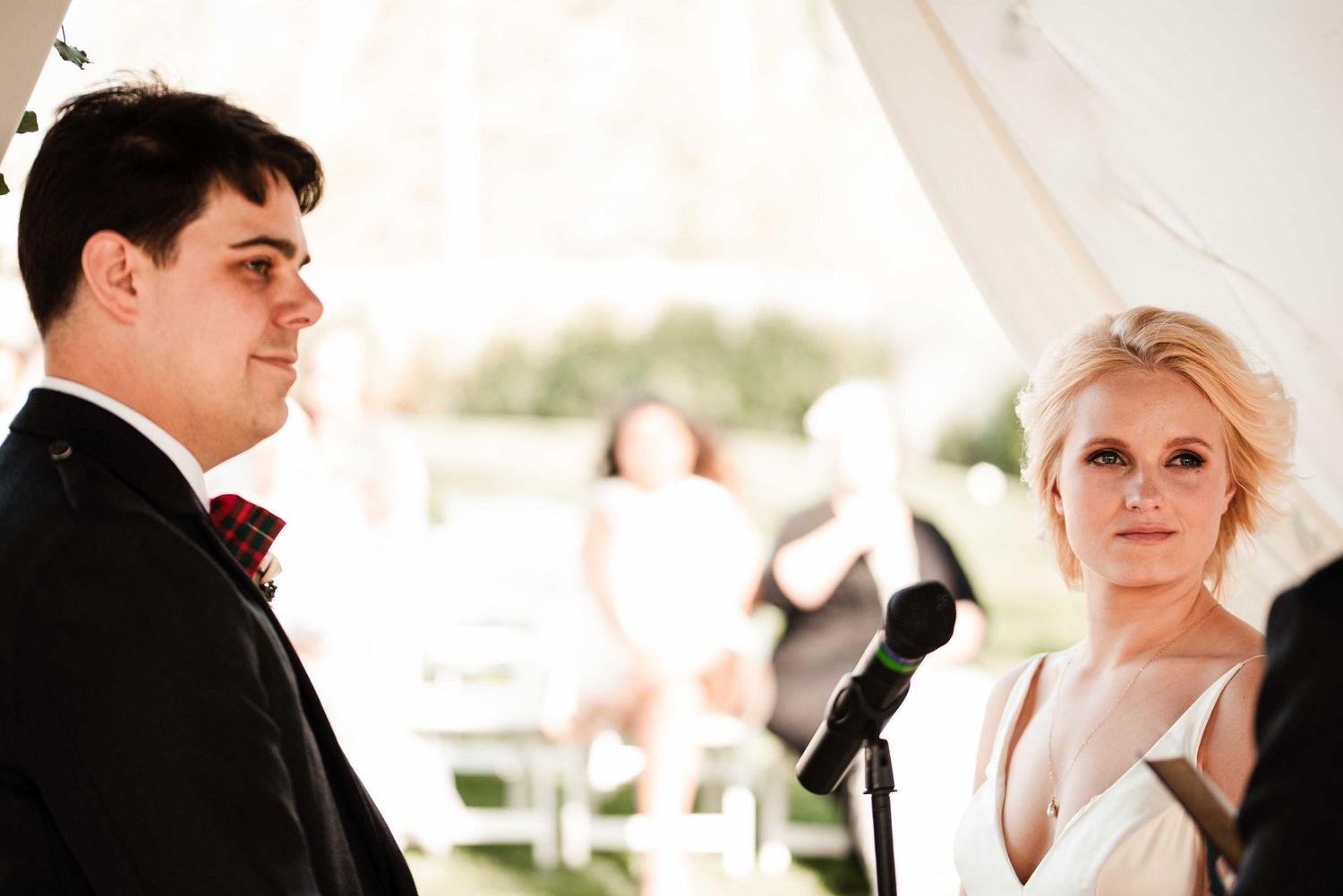 Bride and groom exchange vows at outdoor wedding ceremony under white tent.