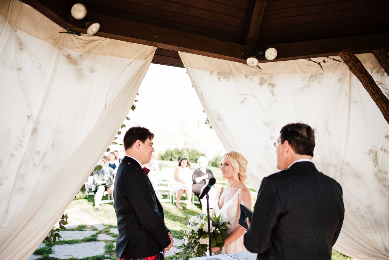 Bride and groom exchange vows under elegant draped canopy at outdoor wedding ceremony.