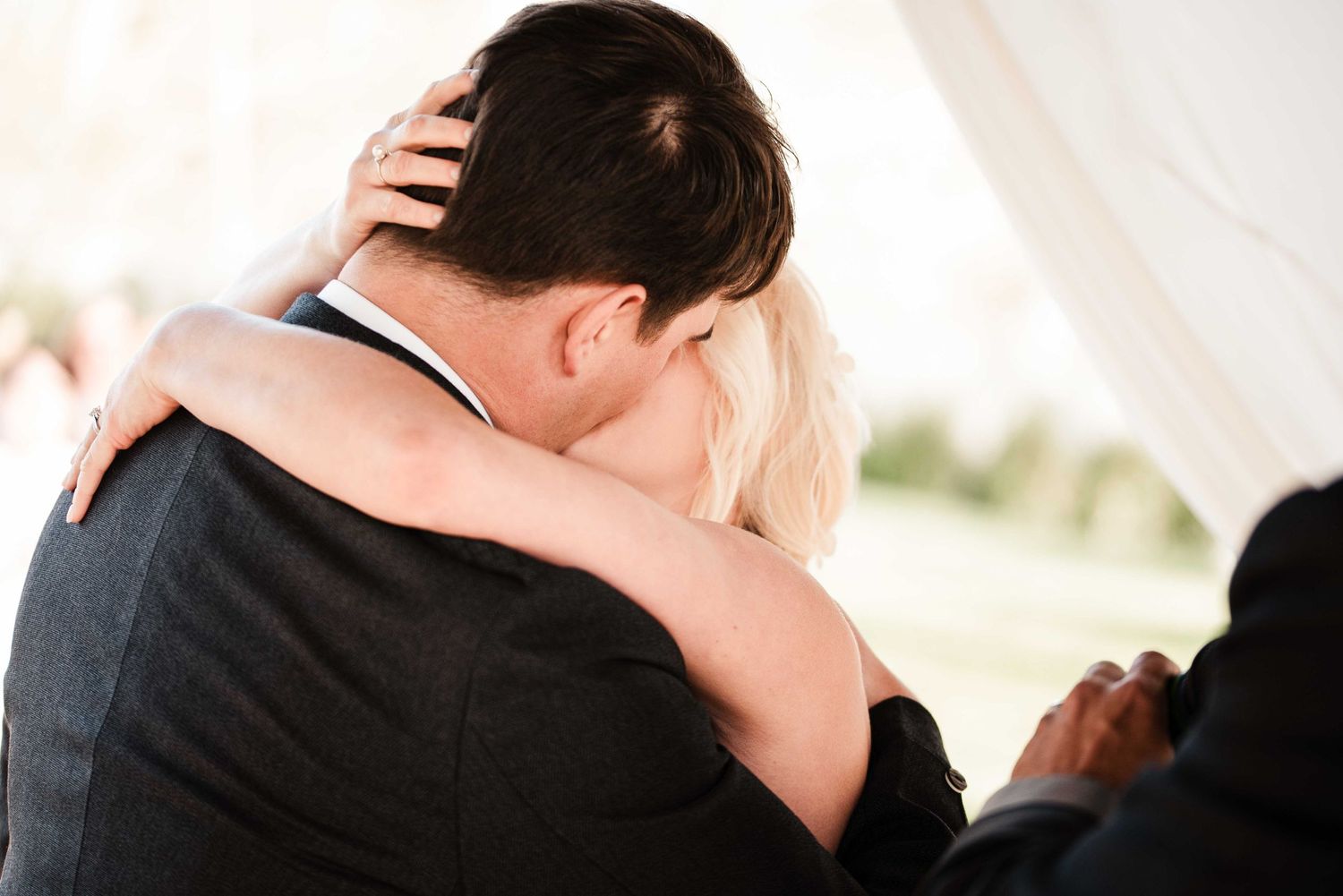 Bride and groom sharing an emotional embrace during wedding ceremony, viewed from behind.