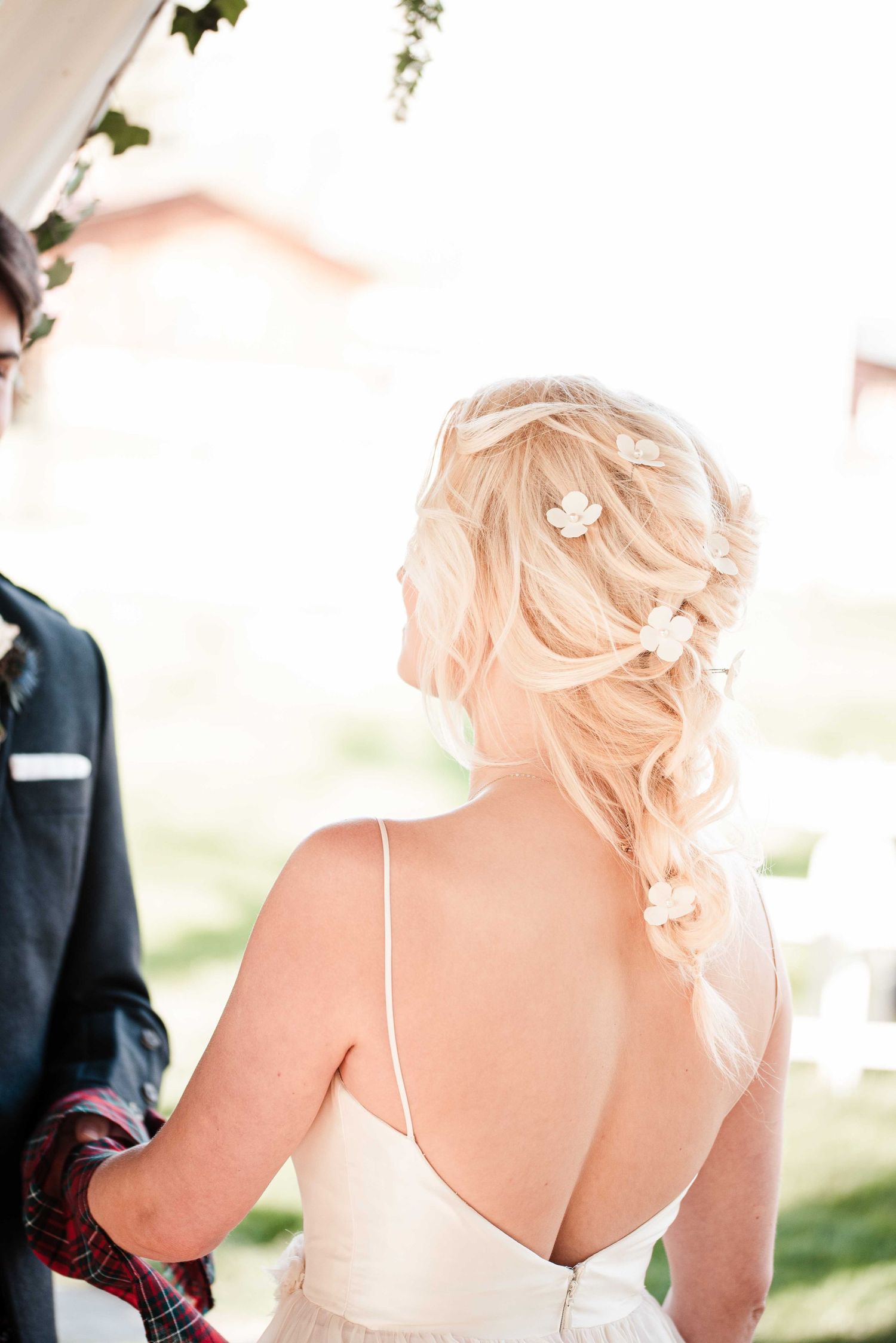 Bride with blonde hair in elegant half-up style adorned with floral pins, wearing a backless white wedding gown.