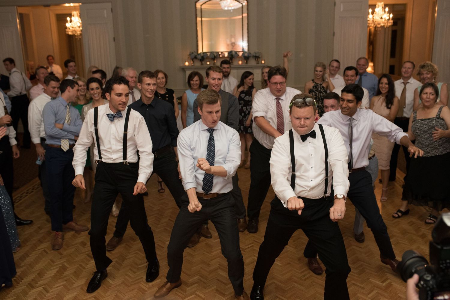 Groomsmen perform energetic dance moves on a grand ballroom dance floor at wedding reception.