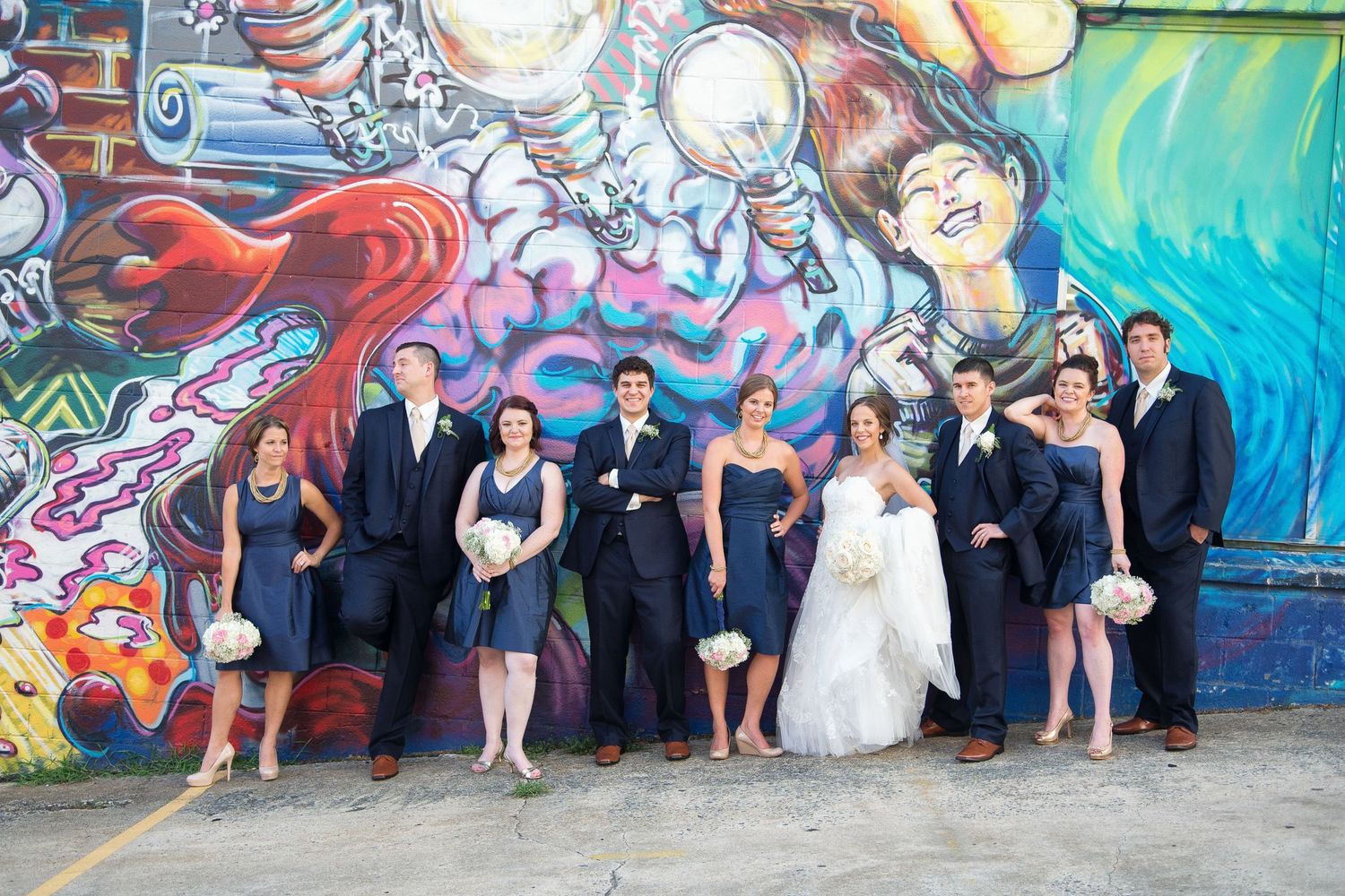 Wedding party poses in navy attire before a vibrant colorful graffiti mural wall.