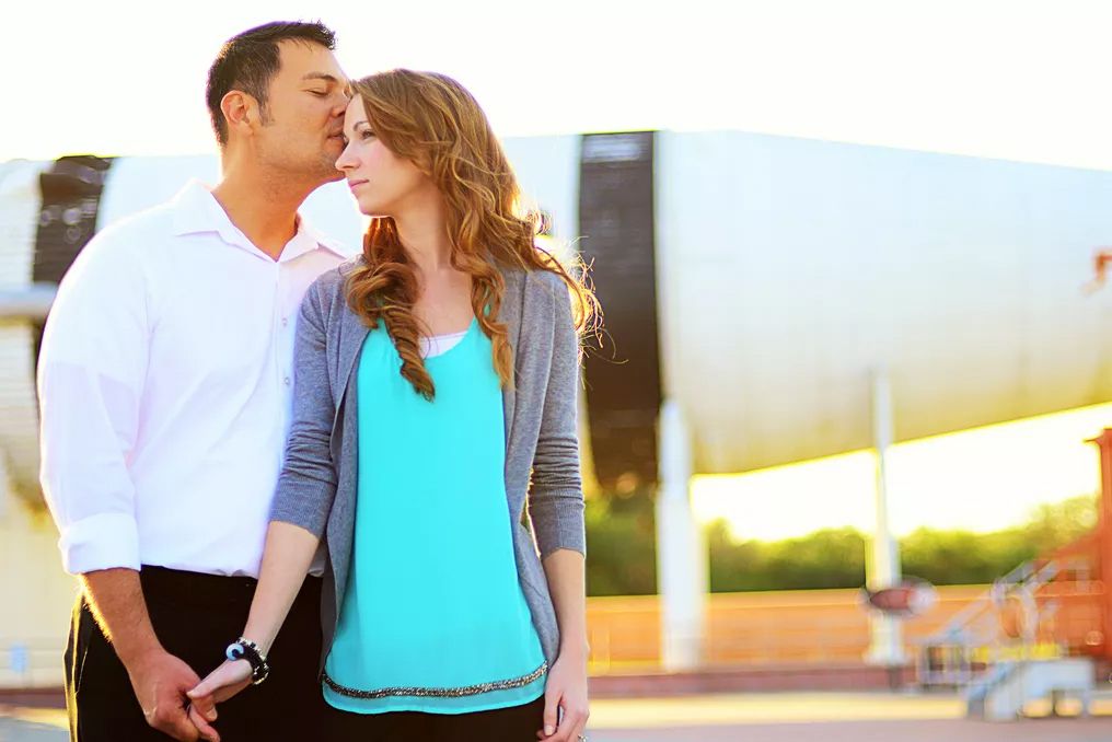 Couple sharing a romantic moment outdoors, holding hands near a modern architectural structure.