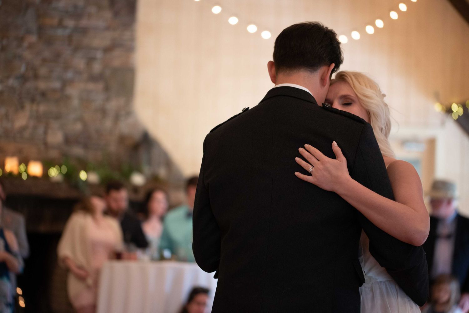 A couple shares their first dance at a wedding reception in a rustic venue with string lights.