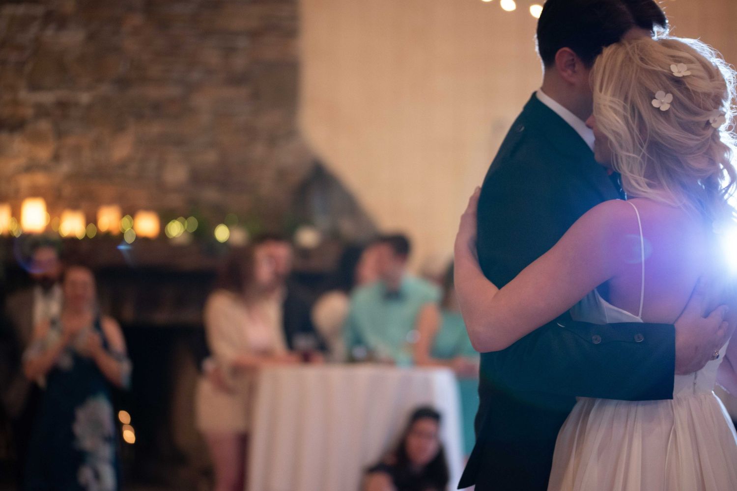 Bride and groom share their first dance at a romantic wedding reception with candlelit stone fireplace backdrop.