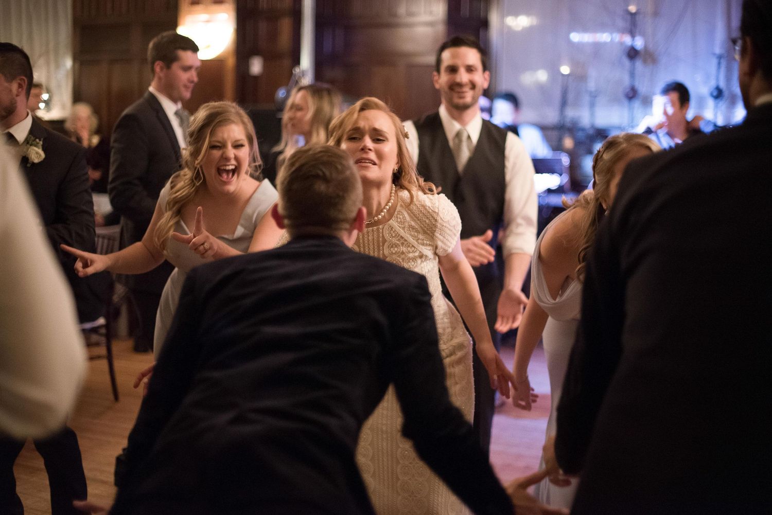 Guests dancing joyfully at a wedding reception in an elegant venue, with bride in white dress.