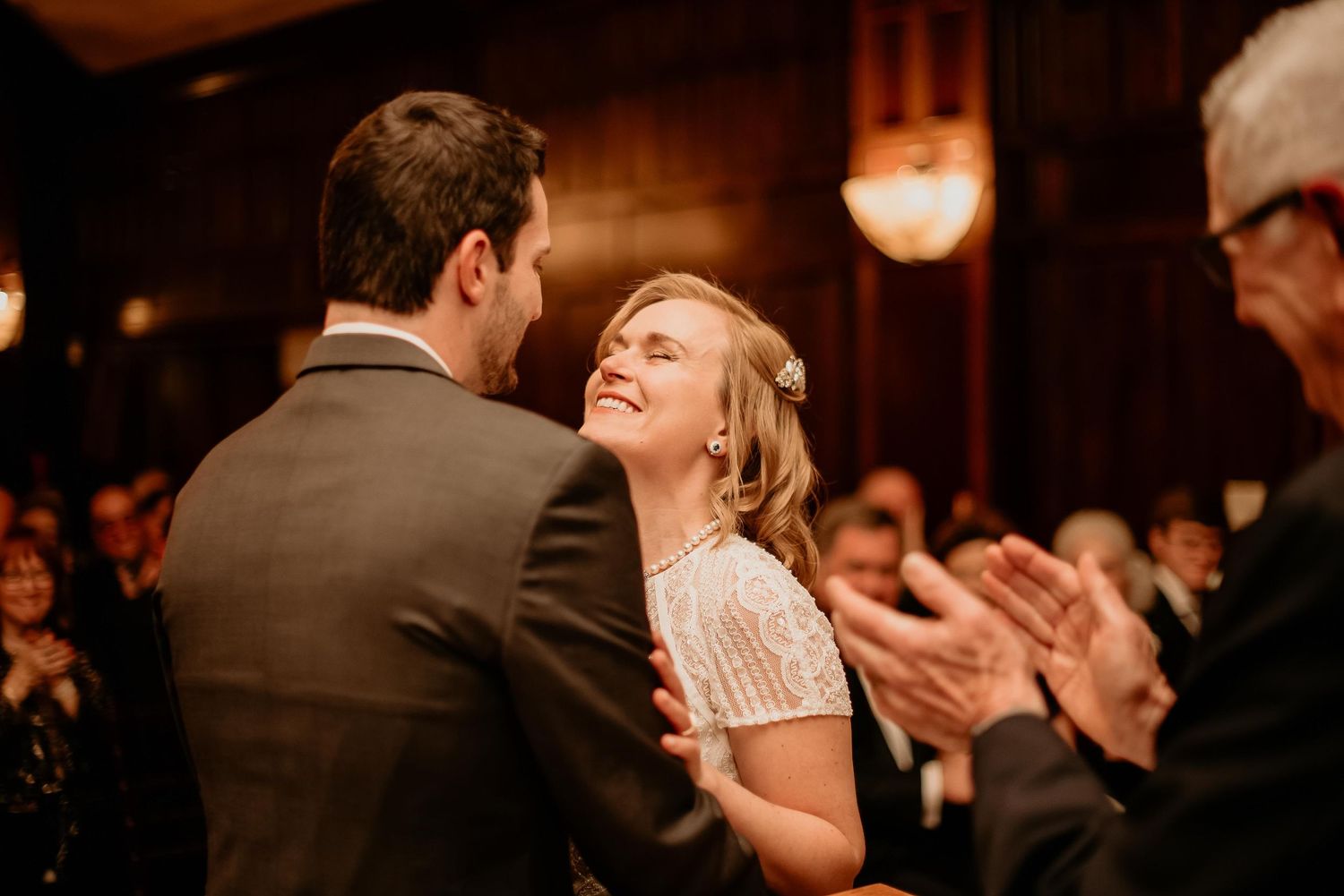 Bride and groom sharing first dance at elegant wedding reception with guests applauding in warm ambient lighting.