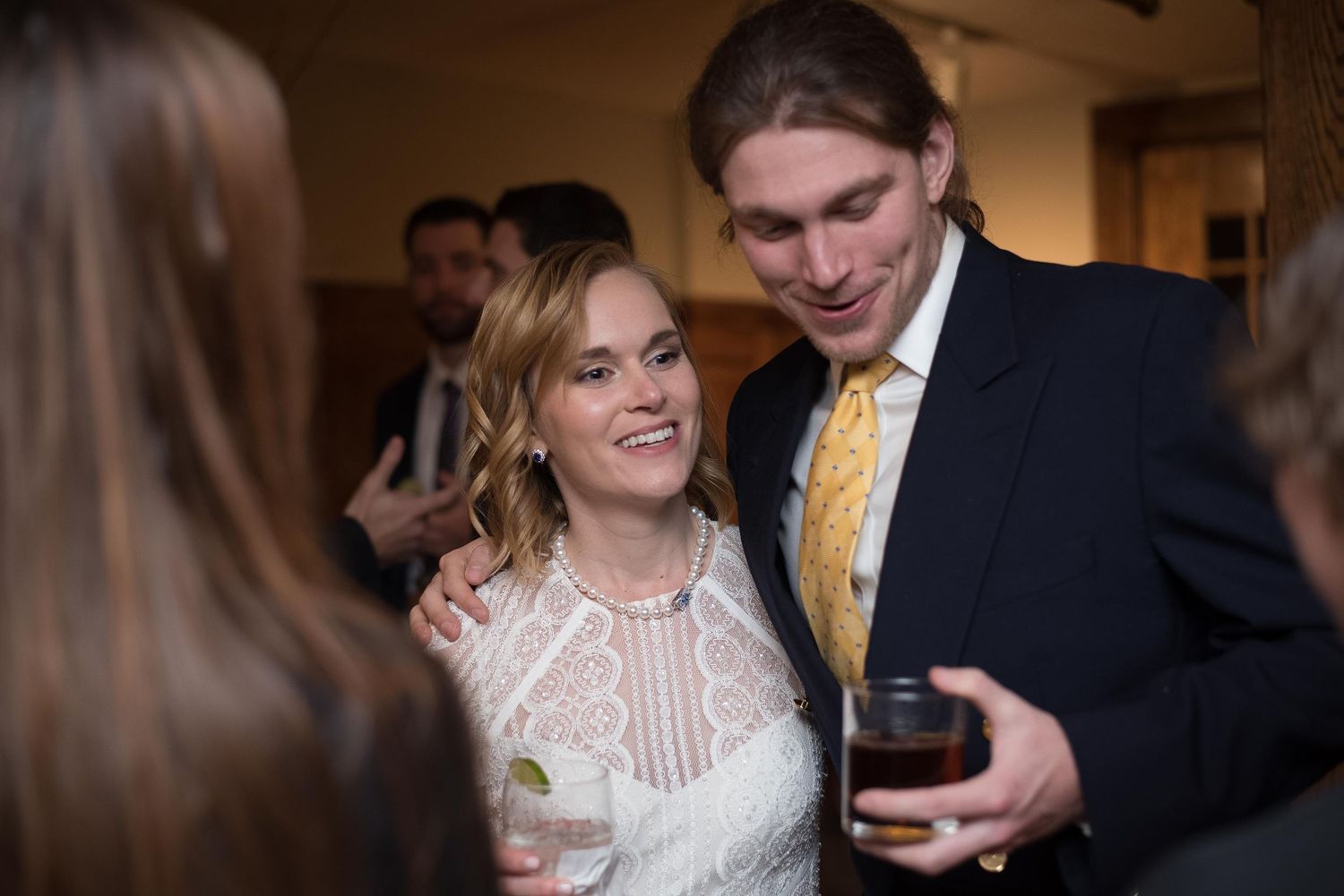 A smiling couple poses together at a formal event, woman in white lace dress, man in dark suit with yellow tie.