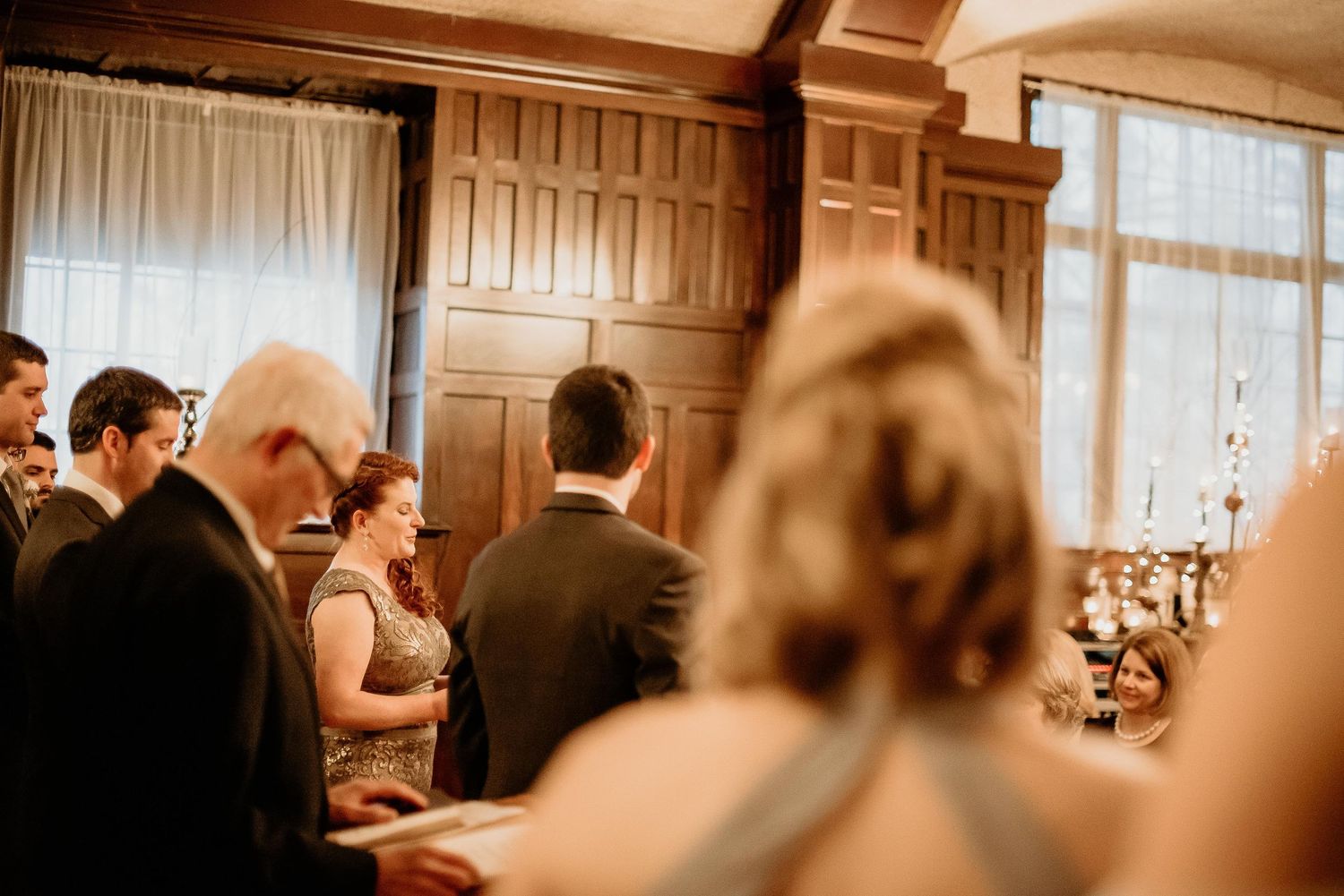 Guests mingle in an elegant wood-paneled reception hall during a formal wedding gathering.