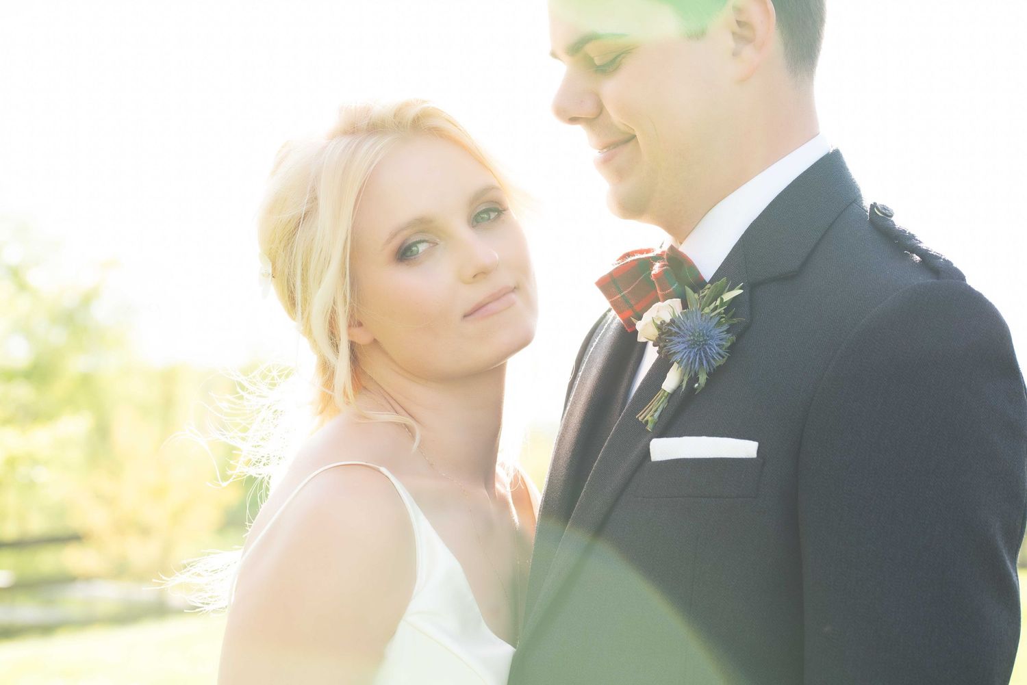 Beautiful blonde bride gazes at groom in soft golden sunlight during outdoor wedding portrait.