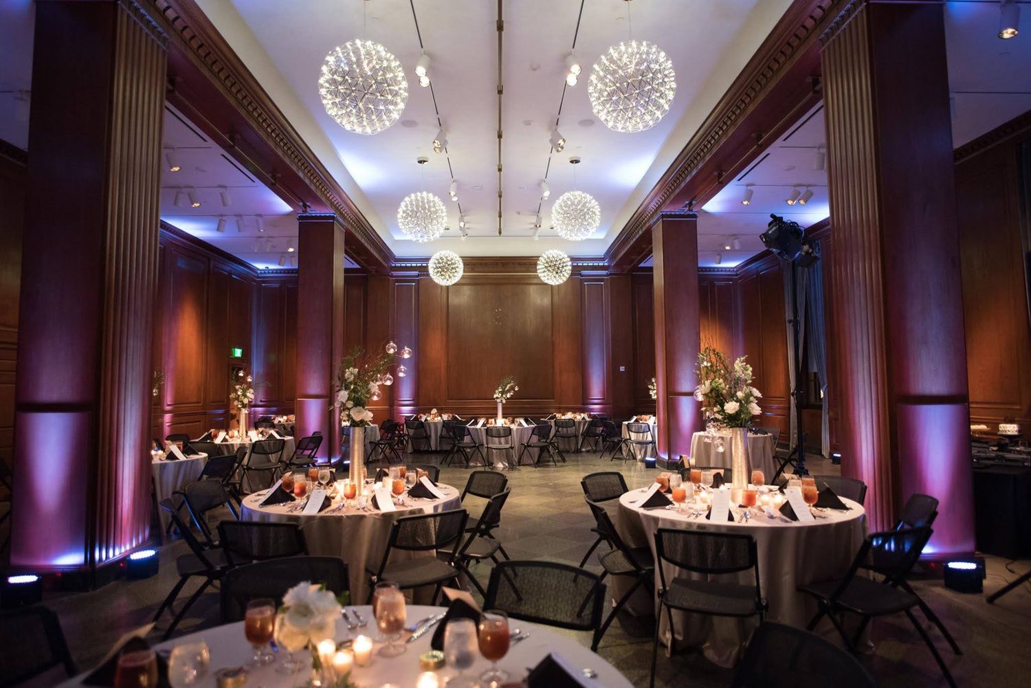 Elegant wedding reception hall with globe chandeliers and candlelit round tables.
