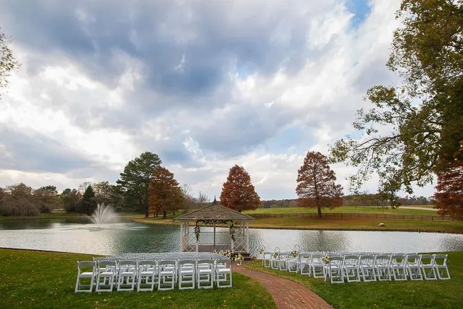 Outdoor wedding ceremony setup with white chairs beside a tranquil pond with a fountain.