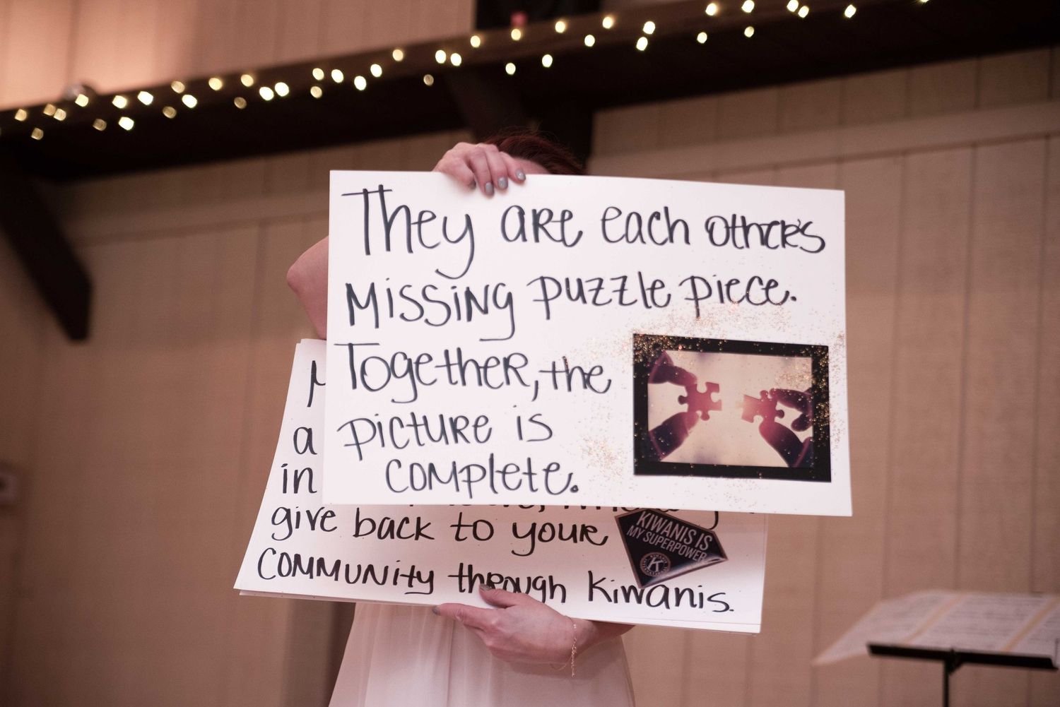 Person holding a handwritten sign about missing puzzle pieces and community involvement through Kiwanis at an event.
