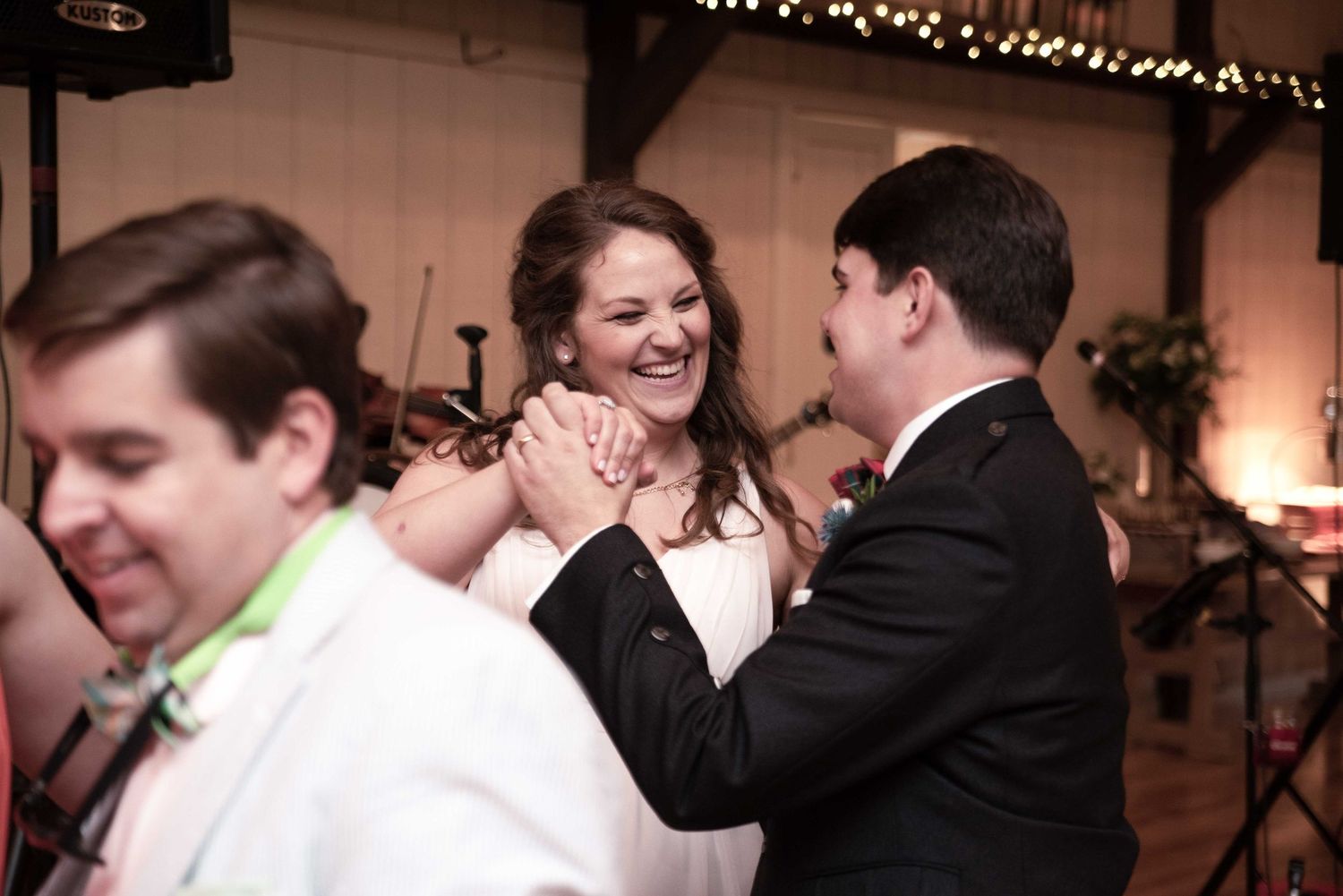 Bride and groom laughing and dancing together at their wedding reception in a rustic barn venue.