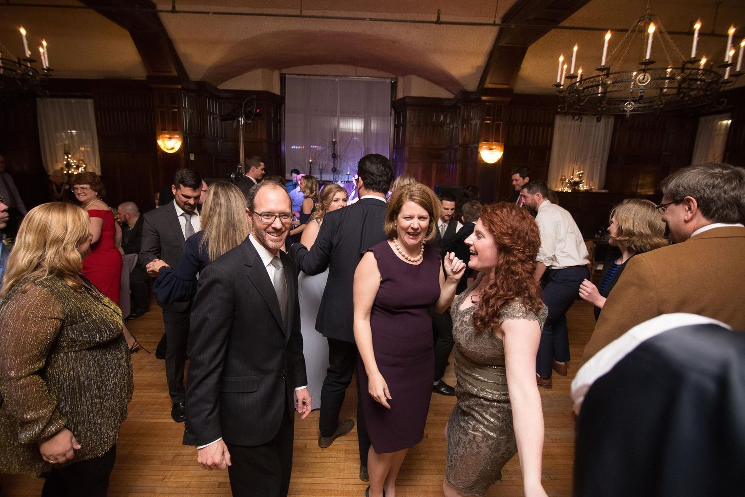 Guests dancing and socializing at an elegant indoor wedding reception in a candlelit ballroom.
