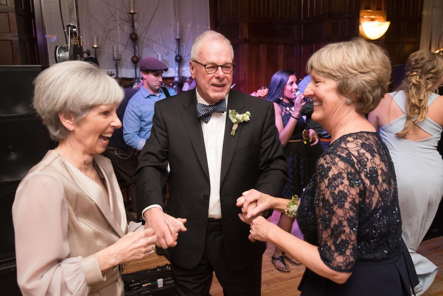Three elegantly dressed guests smiling and chatting at a formal wedding reception event.