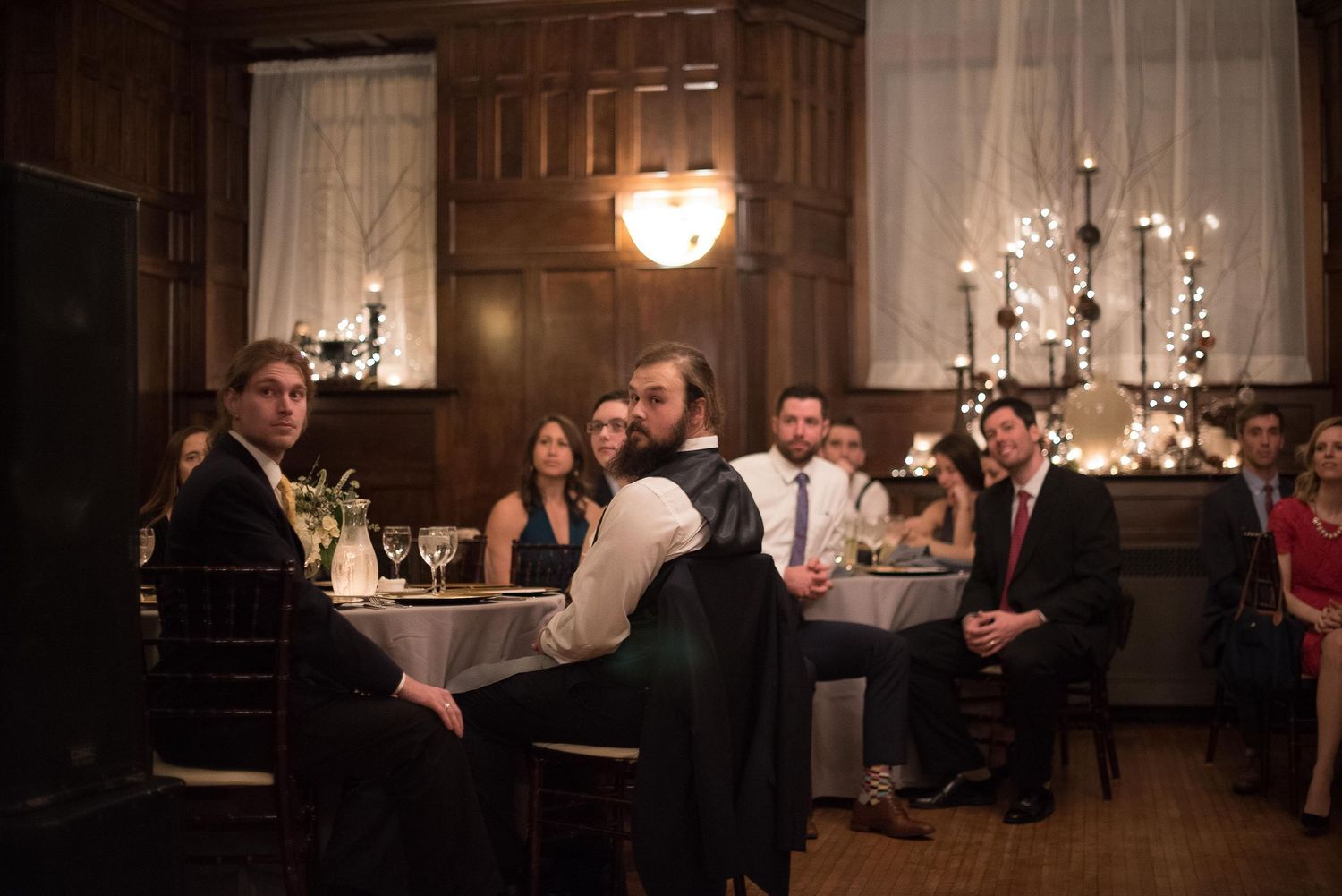 Guests seated at candlelit tables in an elegant wood-paneled banquet hall during a formal dinner event.