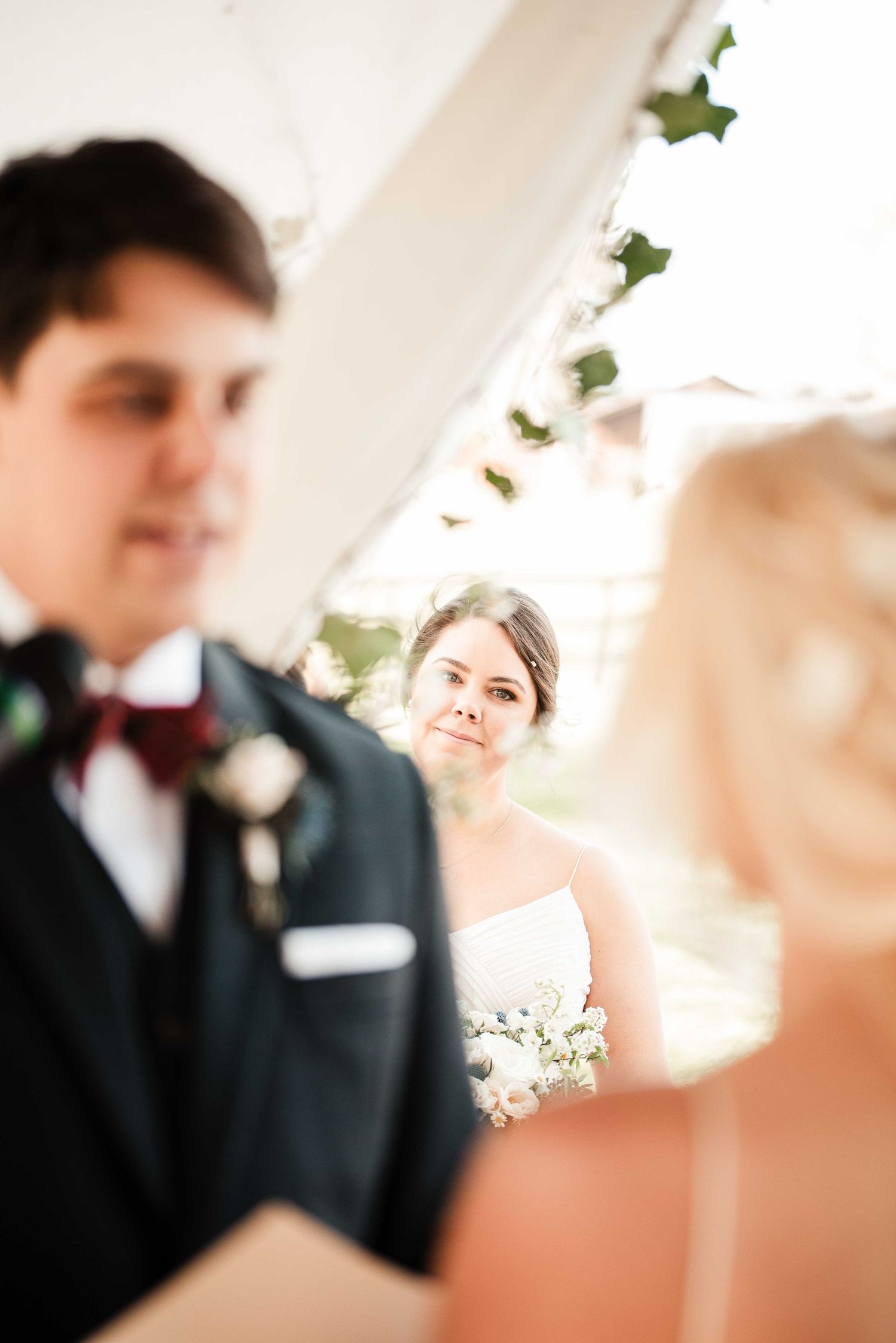 Bride gazes lovingly at groom during outdoor wedding ceremony under white tent with ivy decorations.