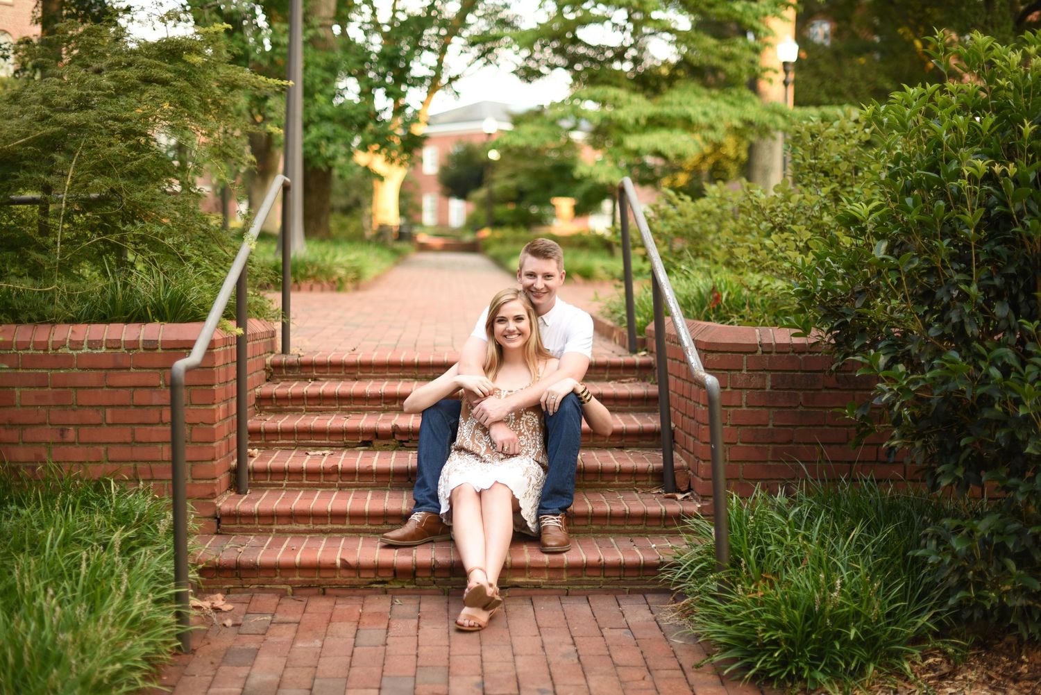 Couple sitting together on brick steps surrounded by green landscaping.