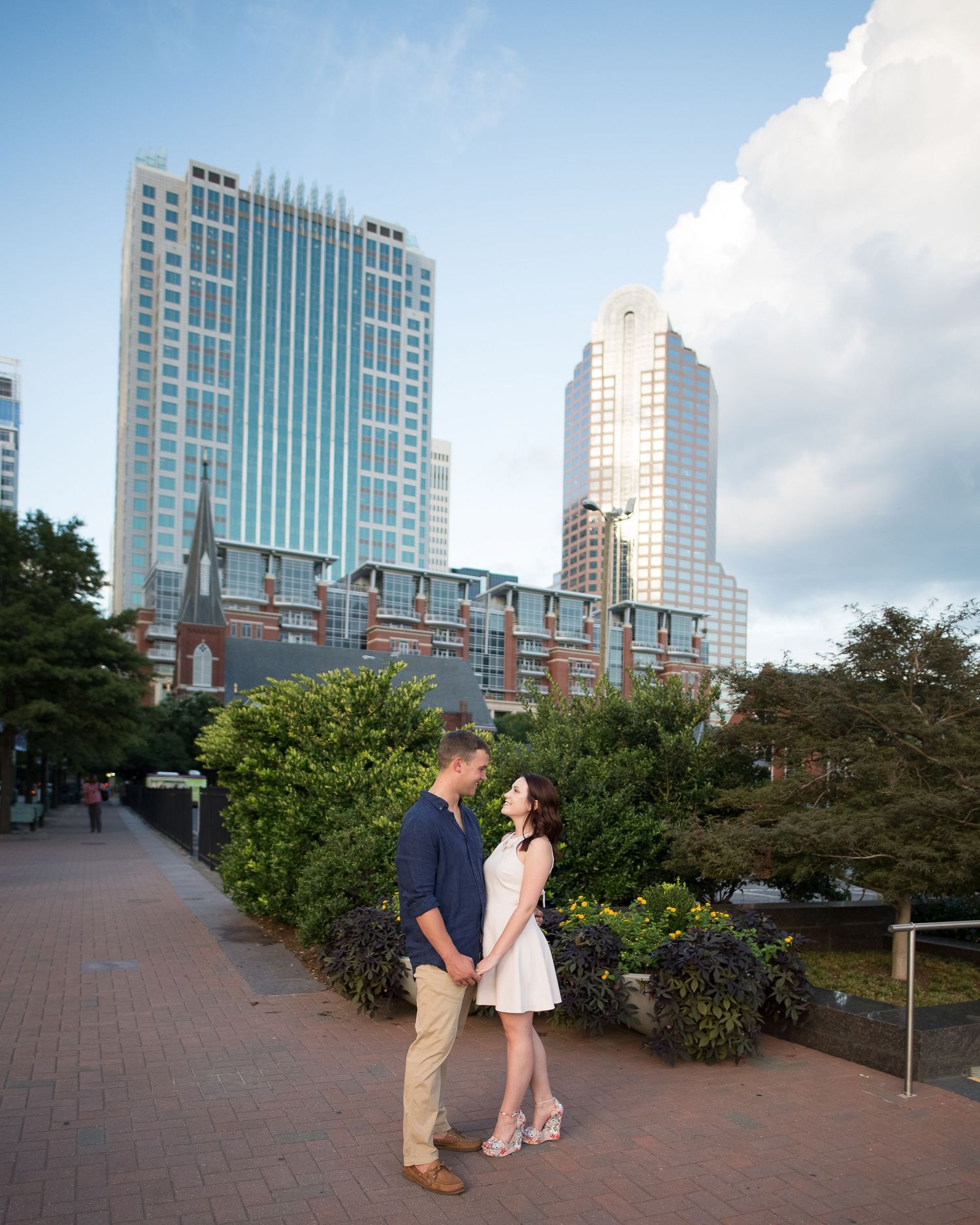 Couple sharing a romantic moment on a city walkway with tall modern skyscrapers in background.